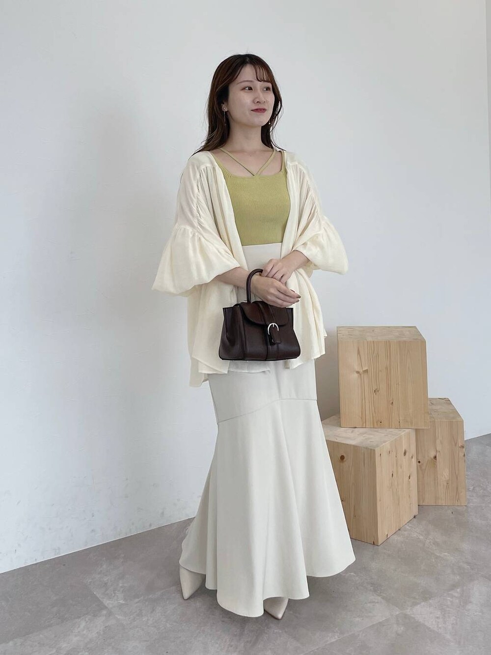 イエロー系のニット/セーター、ブラウン系のハンドバッグ、ホワイト系のシャツ/ブラウスを着用したレディースの夏コーディネートの2枚目の写真
