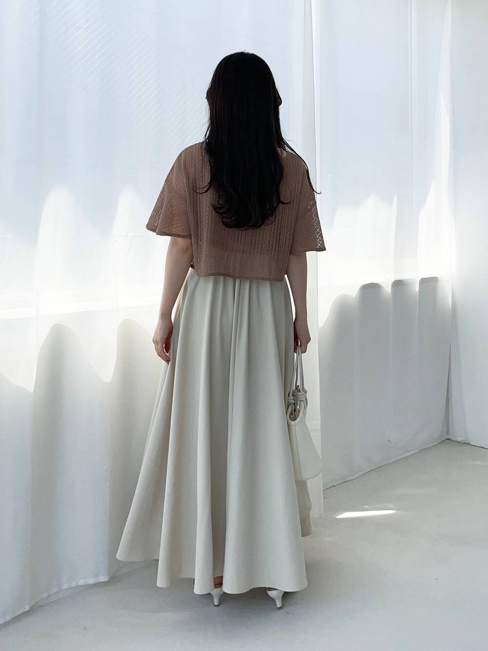 ホワイト系のハンドバッグ、ブラウン系のカーディガン/ボレロ、ホワイト系のサンダルを着用したレディースの夏コーディネートの2枚目の写真