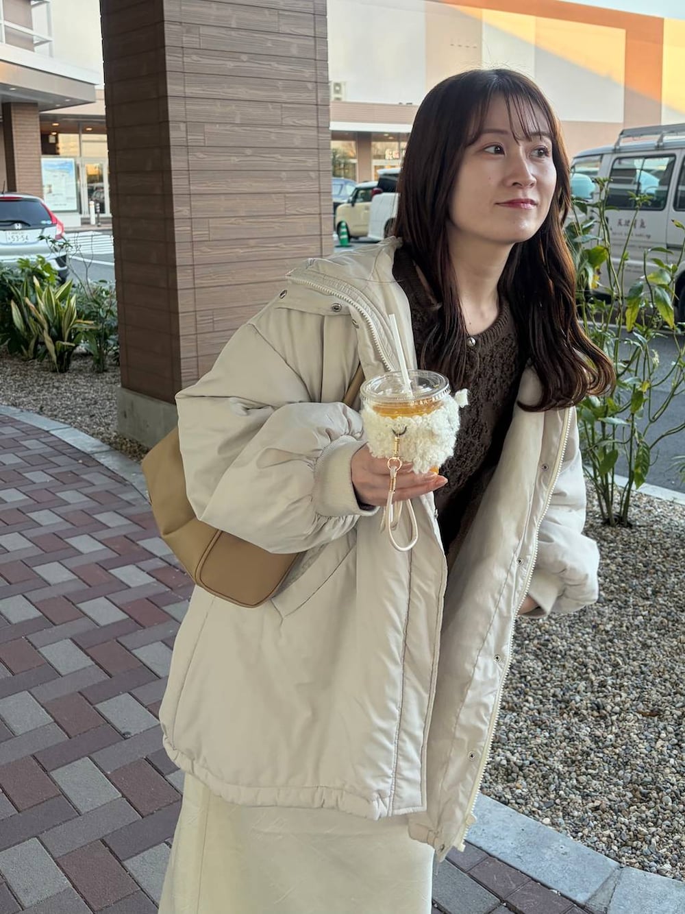 ホワイト系のスカート、ゴールド系のボストンバッグ、ブラウン系のカーディガン/ボレロを着用したレディースの冬コーディネートの3枚目の写真