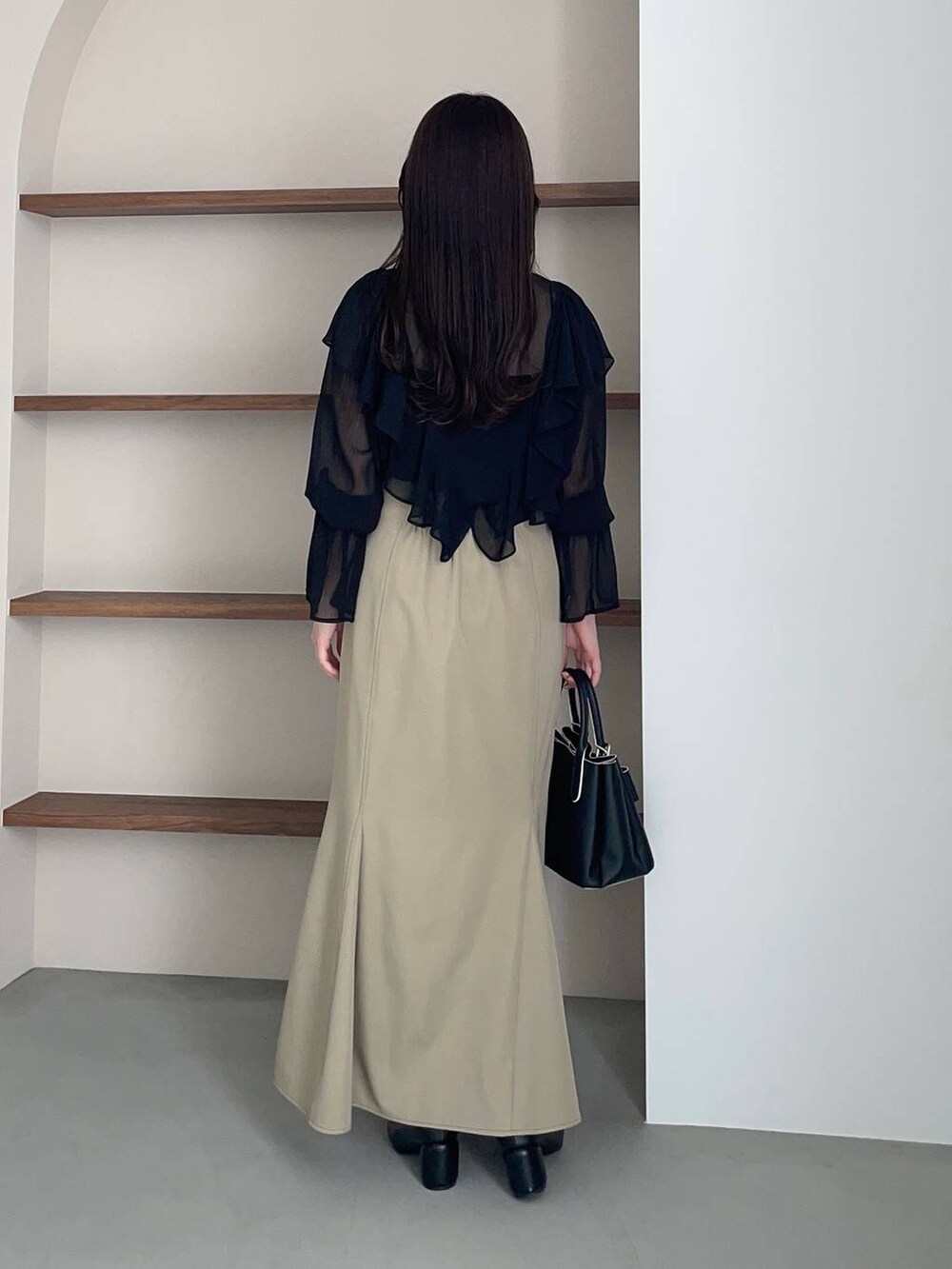 ブラック系のショルダーバッグ、ブラック系のパンプス、ベージュ系のスカートを着用したレディースの春コーディネートの2枚目の写真