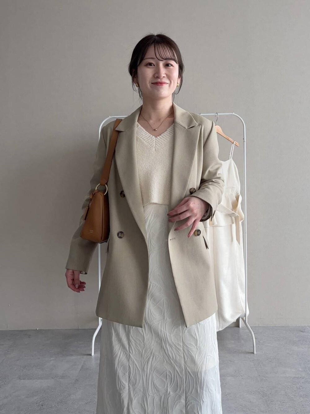 ブルー系のデニムパンツ、ベージュ系のテーラードジャケット、ホワイト系のニット/セーターを着用したレディースの春コーディネートの3枚目の写真