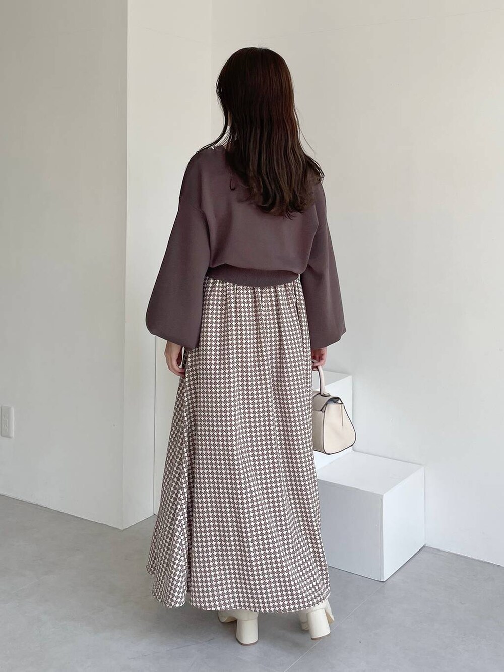 ホワイト系のハンドバッグ、ホワイト系のブーツ、ブラウン系のスカートを着用したレディースの夏コーディネートの2枚目の写真