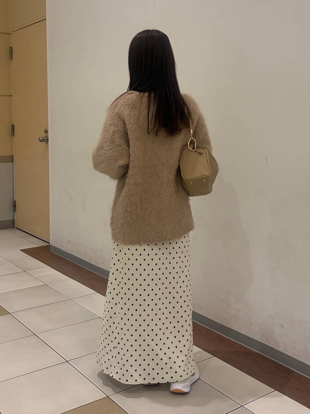 ホワイト系のスカート、ベージュ系のカーディガン/ボレロ、ゴールド系のボストンバッグを着用したレディースの冬コーディネートの2枚目の写真