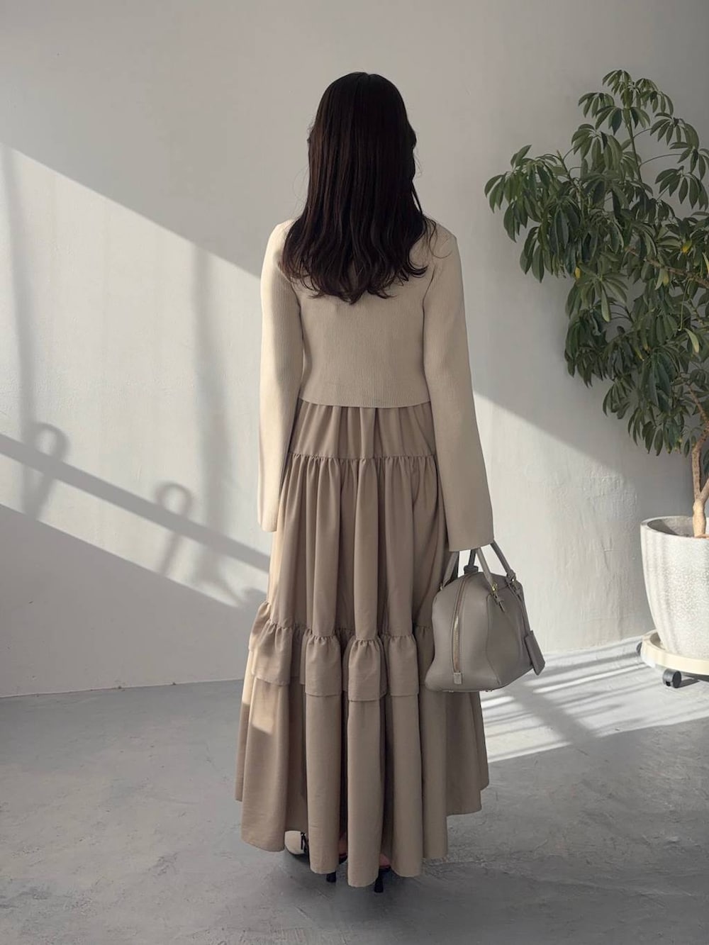 ベージュ系のハンドバッグ、ホワイト系のサンダル、ベージュ系のワンピースを着用したレディースの冬コーディネートの2枚目の写真