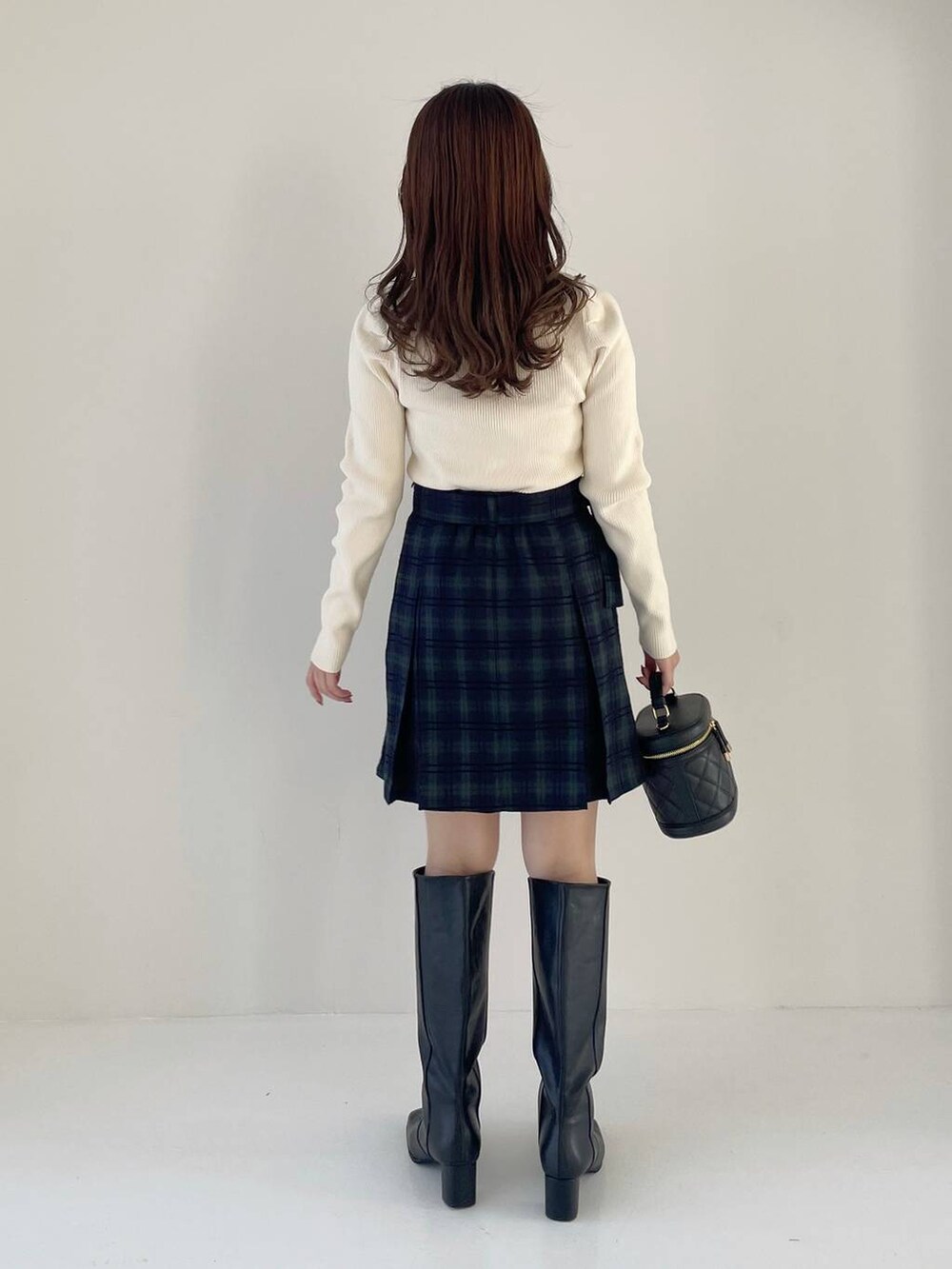 ブラック系のブーツ、ブラック系のショルダーバッグ、ホワイト系のニット/セーターを着用したレディースの秋コーディネートの2枚目の写真