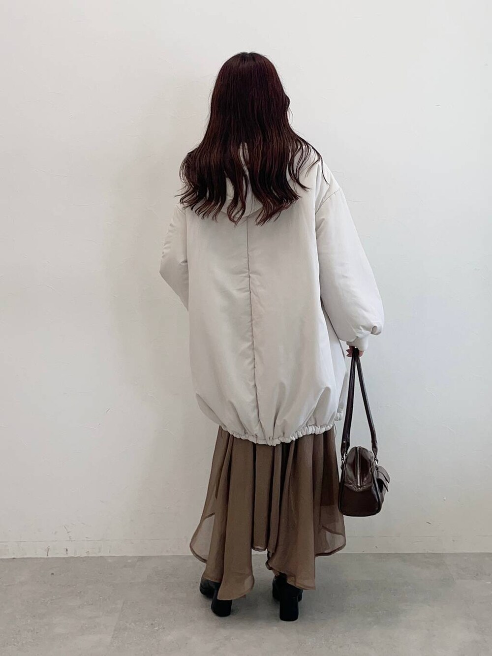 ブラック系のブーツ、ブラウン系のハンドバッグ、ホワイト系のブルゾンを着用したレディースの秋コーディネートの2枚目の写真