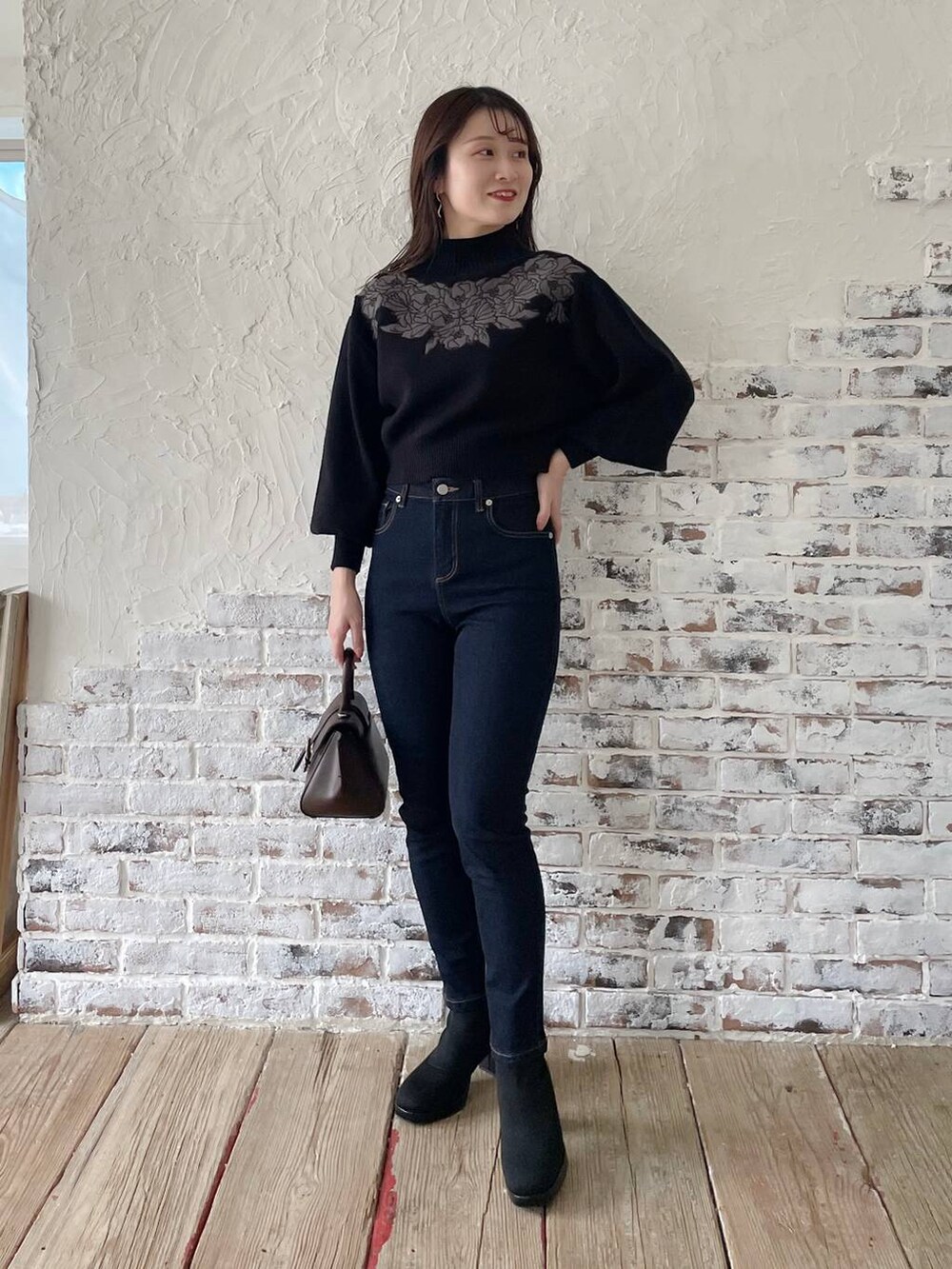 ブルー系のデニムパンツ、ブラウン系のハンドバッグ、ブラック系のブーツを着用したレディースの秋コーディネートの6枚目の写真