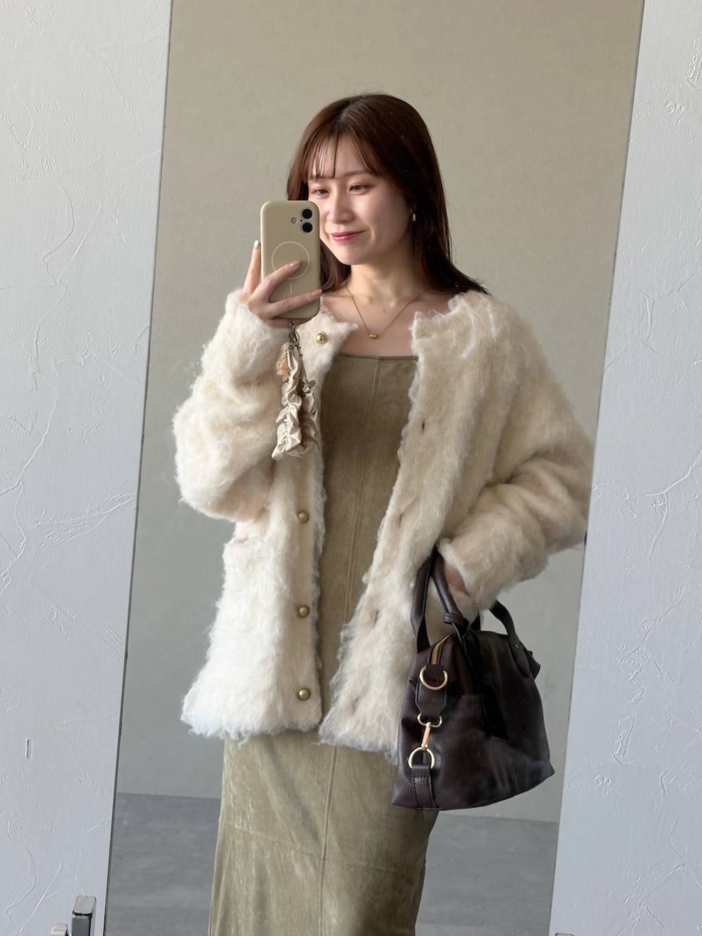 ブラウン系のボストンバッグ、ベージュ系のワンピース、ブラウン系のブーツを着用したレディースの冬コーディネートの3枚目の写真