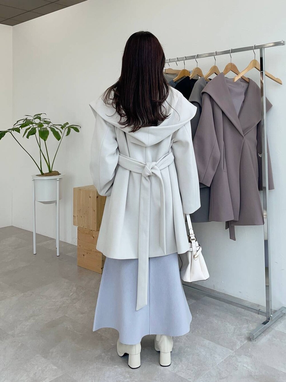 ホワイト系のノーカラーコート、ホワイト系のショルダーバッグ、ホワイト系のブーツを着用したレディースの秋コーディネートの2枚目の写真