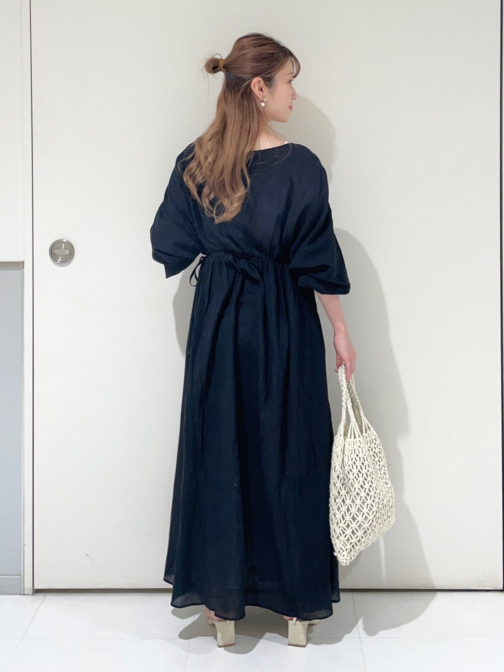 ブラック系のワンピース、ホワイト系のトートバッグ、ホワイト系のサンダルを着用したレディースの夏コーディネートの2枚目の写真