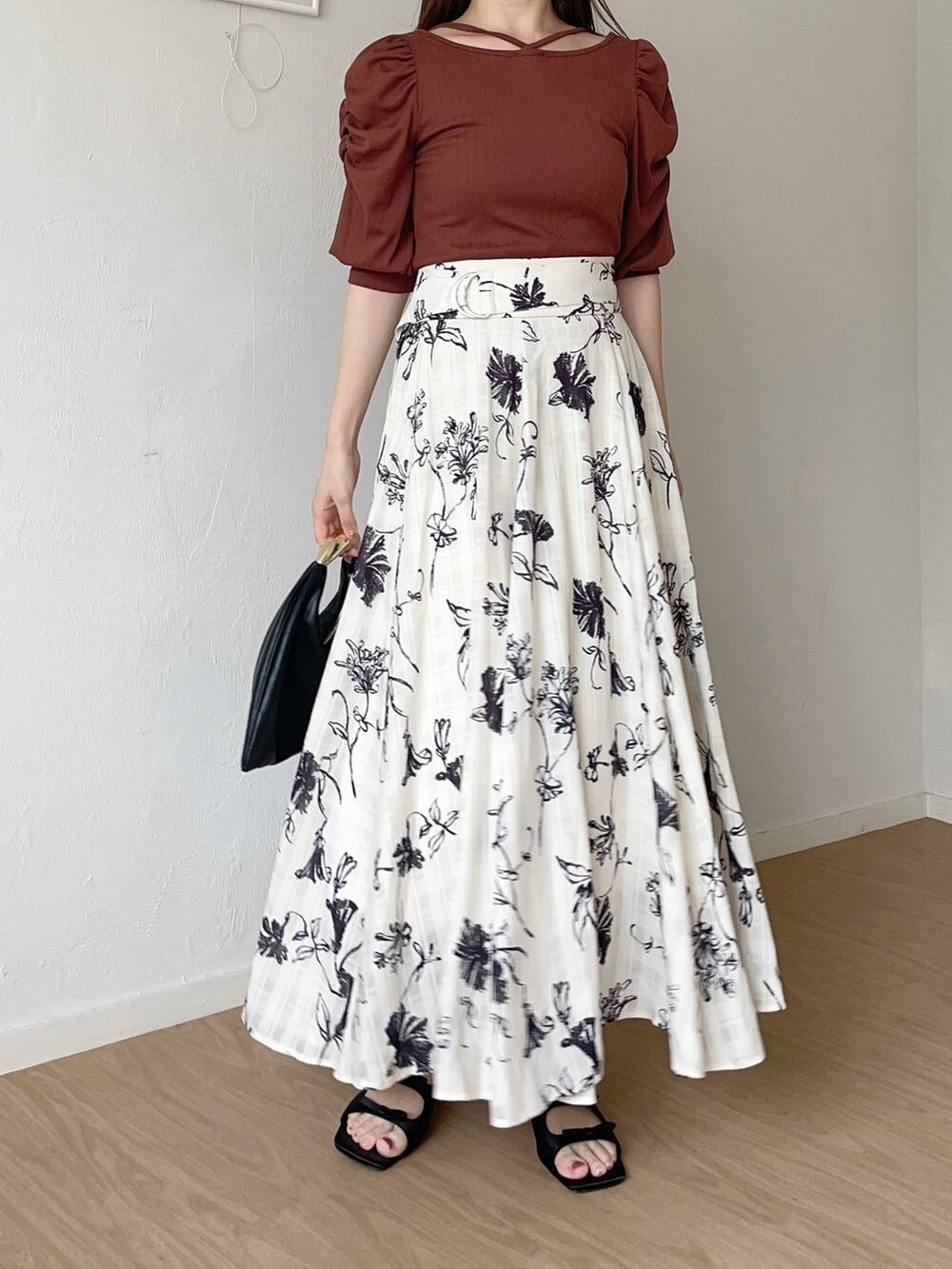 ブラック系のハンドバッグ、ブラウン系のTシャツ/カットソー、ホワイト系のスカートを着用したレディースの秋コーディネートの3枚目の写真