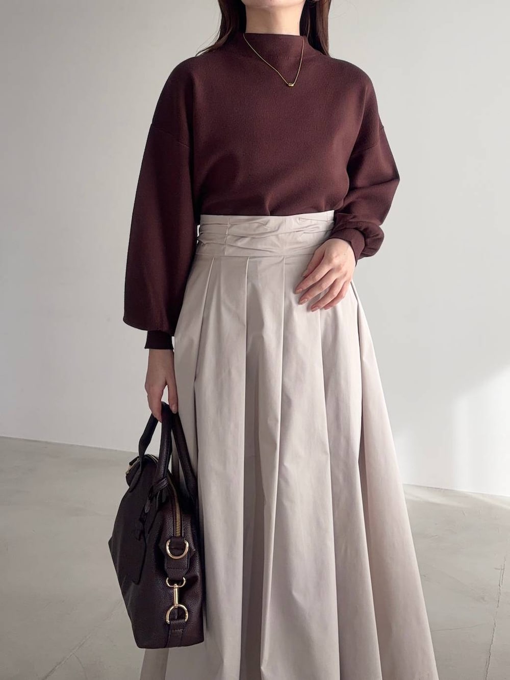 ブラウン系のボストンバッグ、ブラウン系のブーツ、ベージュ系のスカートを着用したレディースの冬コーディネートの3枚目の写真