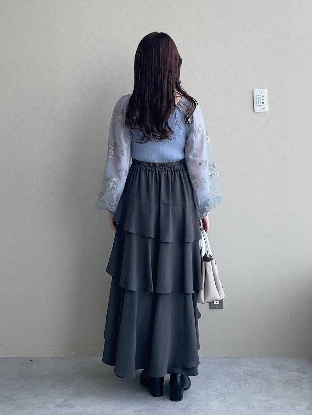 グレー系のスカート、ベージュ系のショルダーバッグ、ブルー系のニット/セーターを着用したレディースの春コーディネートの2枚目の写真