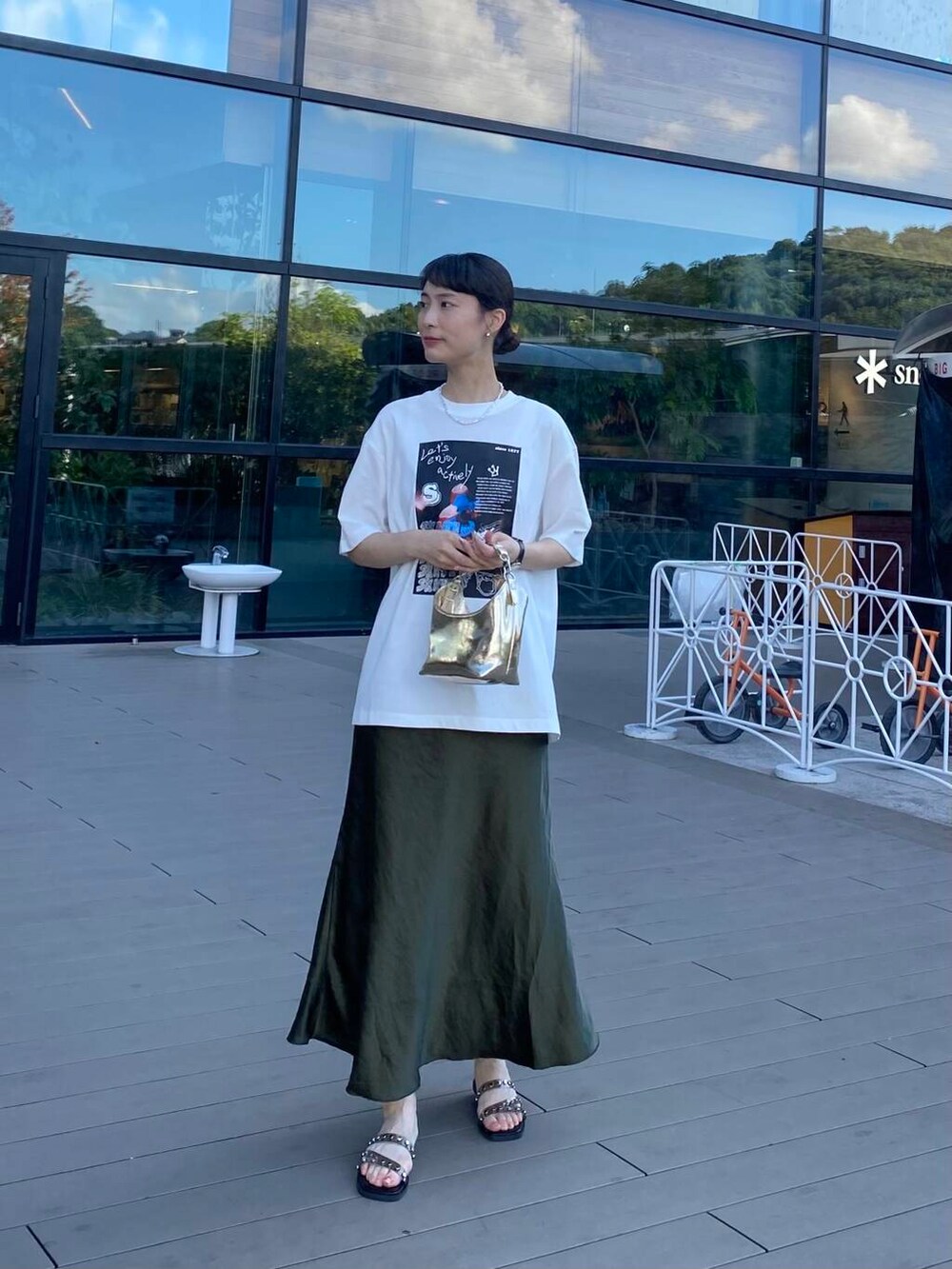 ゴールド系のハンドバッグ、ブラック系のサンダル、ホワイト系のTシャツ/カットソーを着用したレディースの夏コーディネートの4枚目の写真