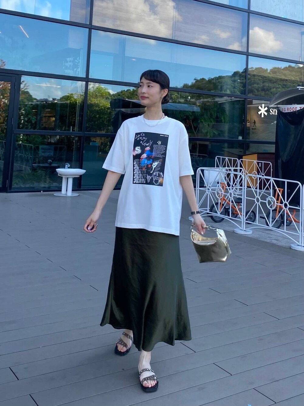 ゴールド系のハンドバッグ、ブラック系のサンダル、ホワイト系のTシャツ/カットソーを着用したレディースの夏コーディネートの3枚目の写真