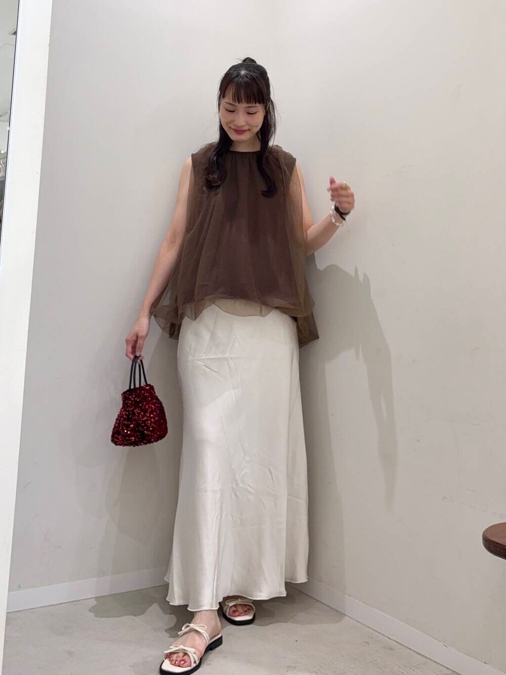 レッド系のショルダーバッグ、ホワイト系のスカート、ホワイト系のタンクトップを着用したレディースの夏コーディネートの3枚目の写真