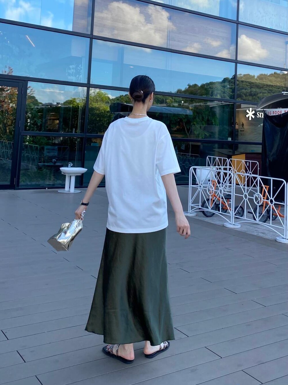 ゴールド系のハンドバッグ、ブラック系のサンダル、ホワイト系のTシャツ/カットソーを着用したレディースの夏コーディネートの2枚目の写真