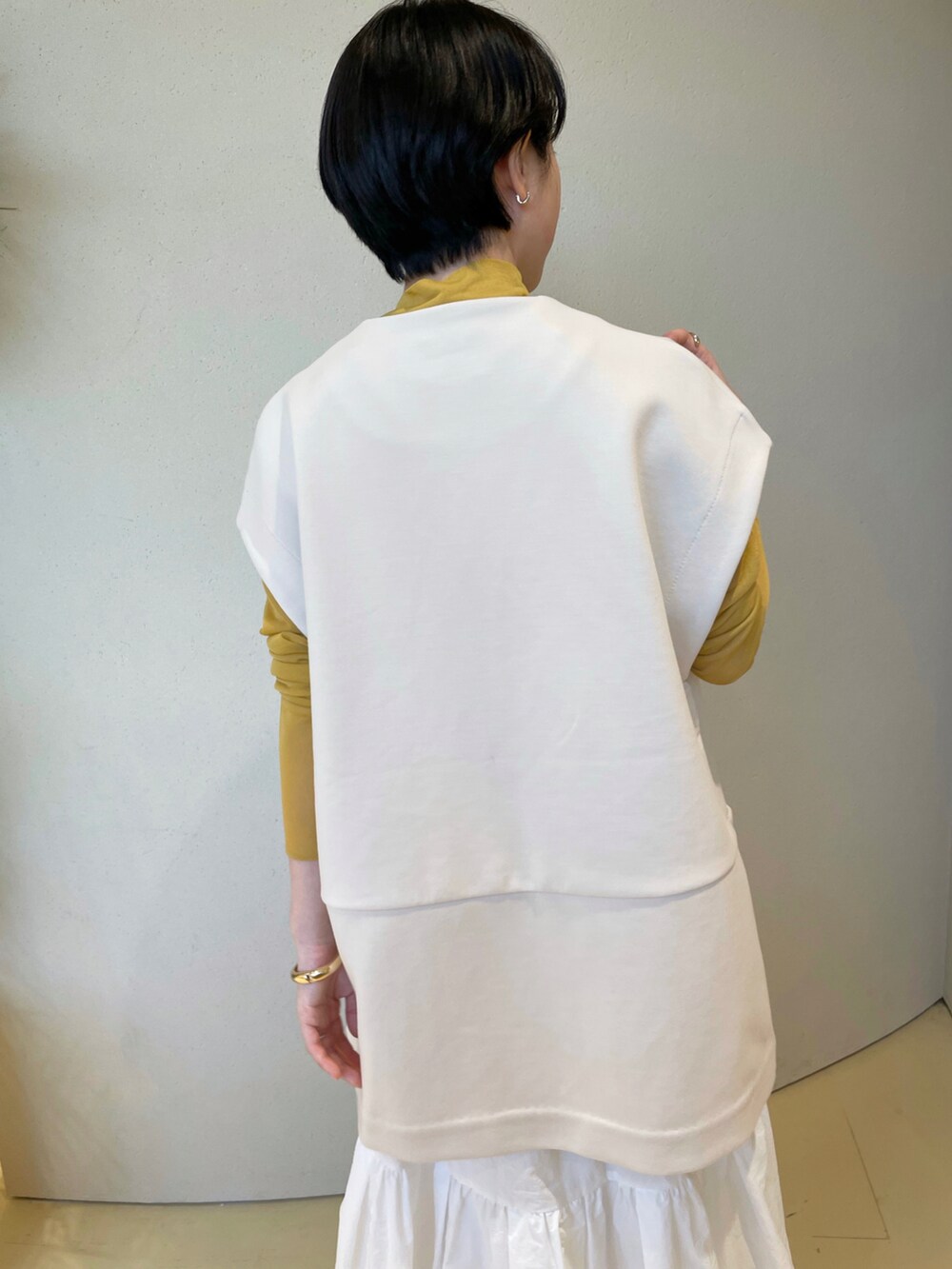 オレンジ系のニット/セーター、ホワイト系のベスト、ホワイト系のスカートを着用したレディースの冬コーディネートの4枚目の写真