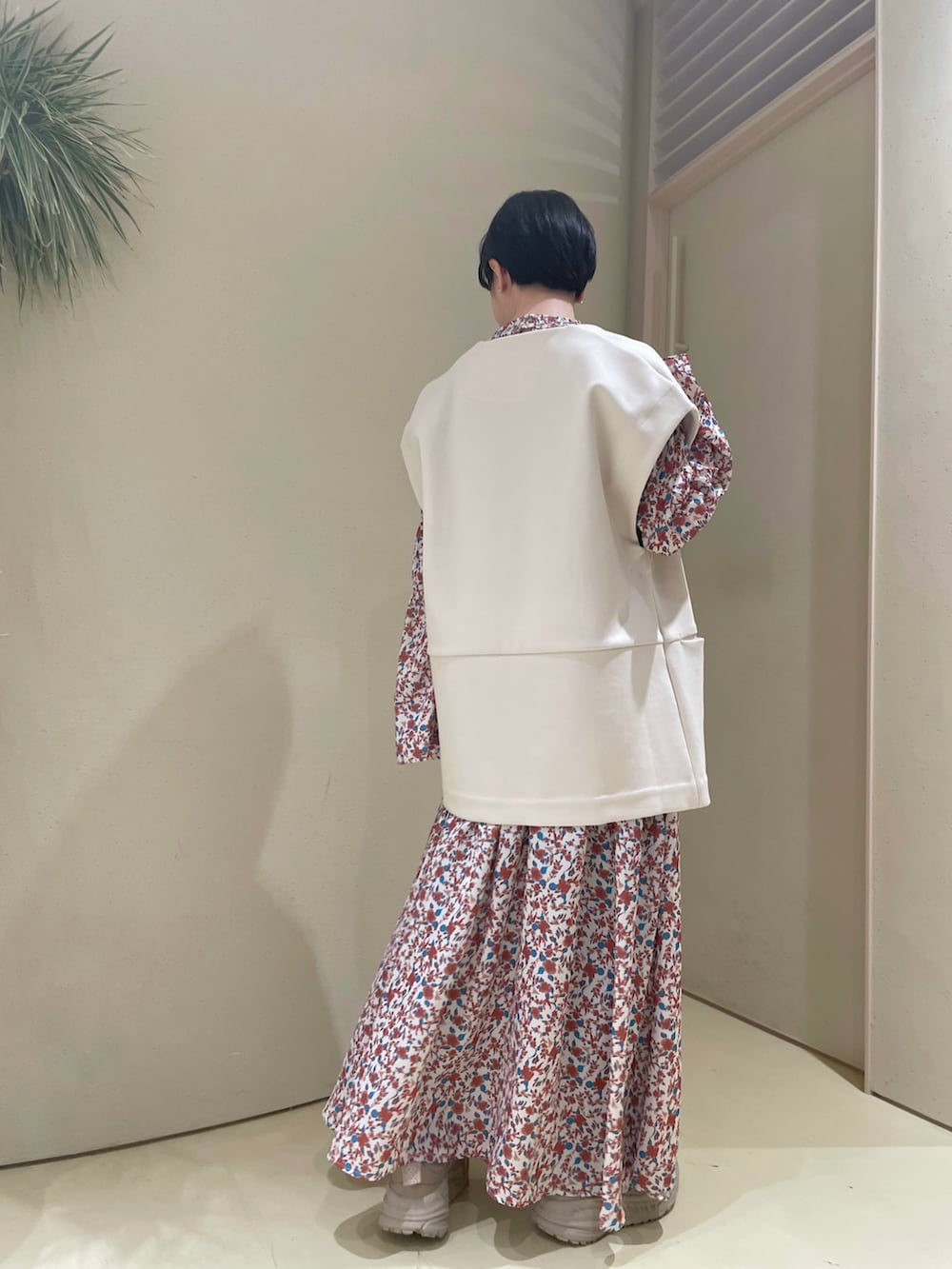 レッド系のワンピース、ホワイト系のベスト、ベージュ系のスニーカーを着用したレディースの春コーディネートの3枚目の写真