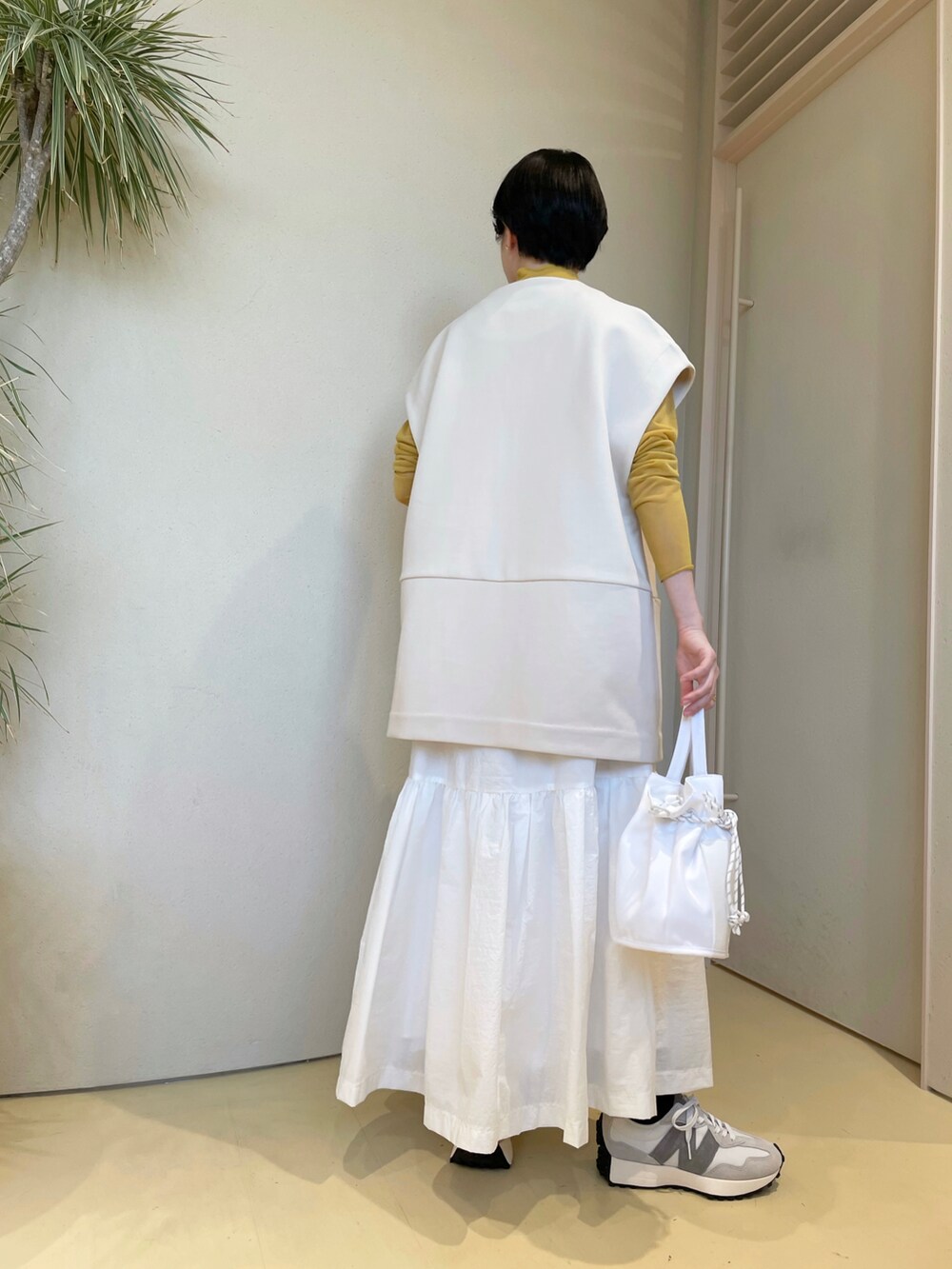 オレンジ系のニット/セーター、ホワイト系のベスト、ホワイト系のスカートを着用したレディースの冬コーディネートの2枚目の写真