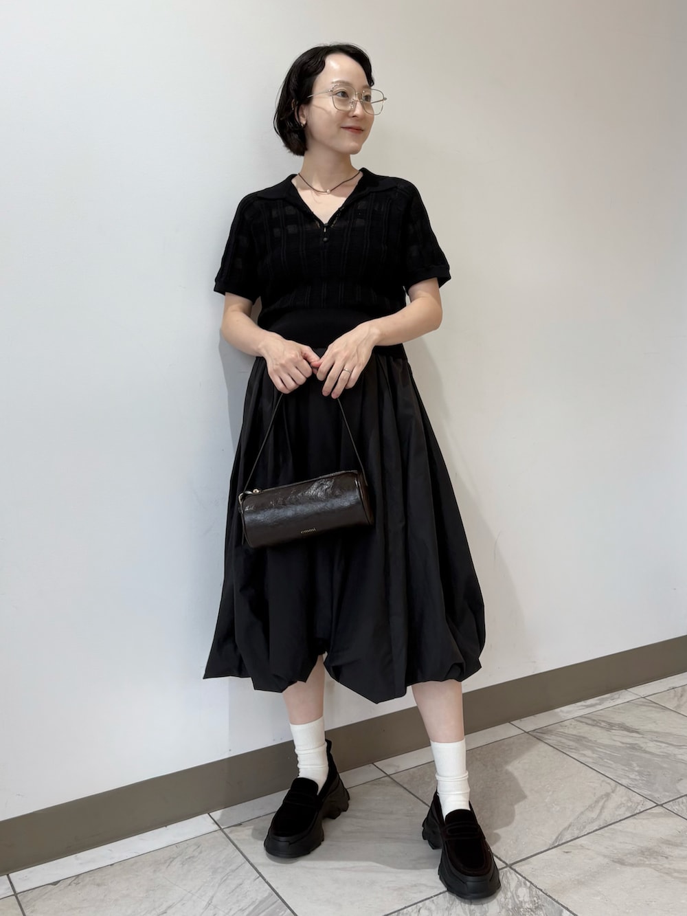 ブラック系のポロシャツ、ブラック系のスカート、ブラウン系のショルダーバッグを着用したレディースの夏コーディネートの2枚目の写真