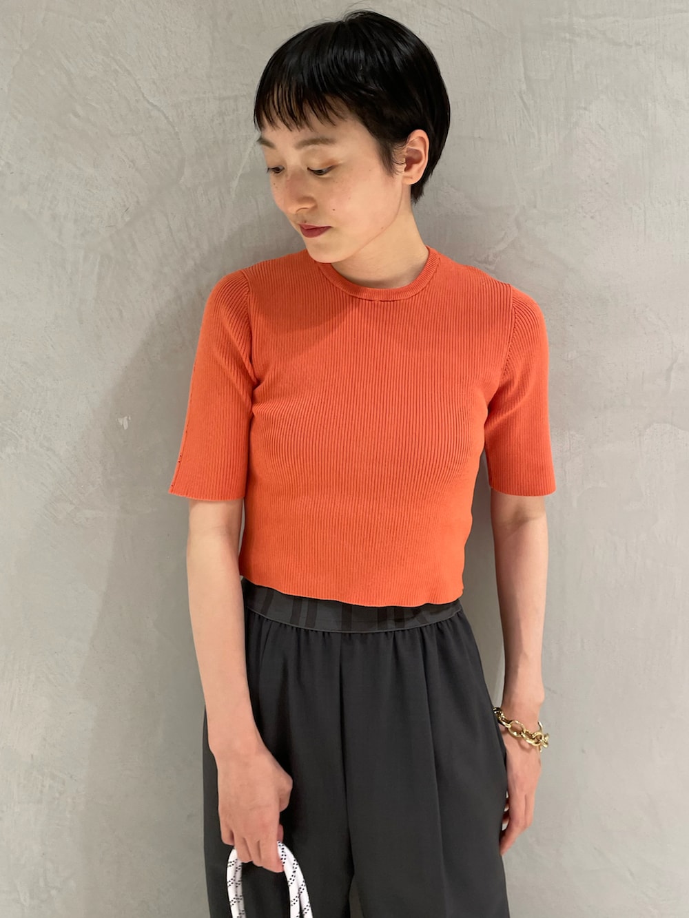 グレー系のスラックス、オレンジ系のニット/セーター、ホワイト系のショルダーバッグを着用したレディースの夏コーディネートの3枚目の写真