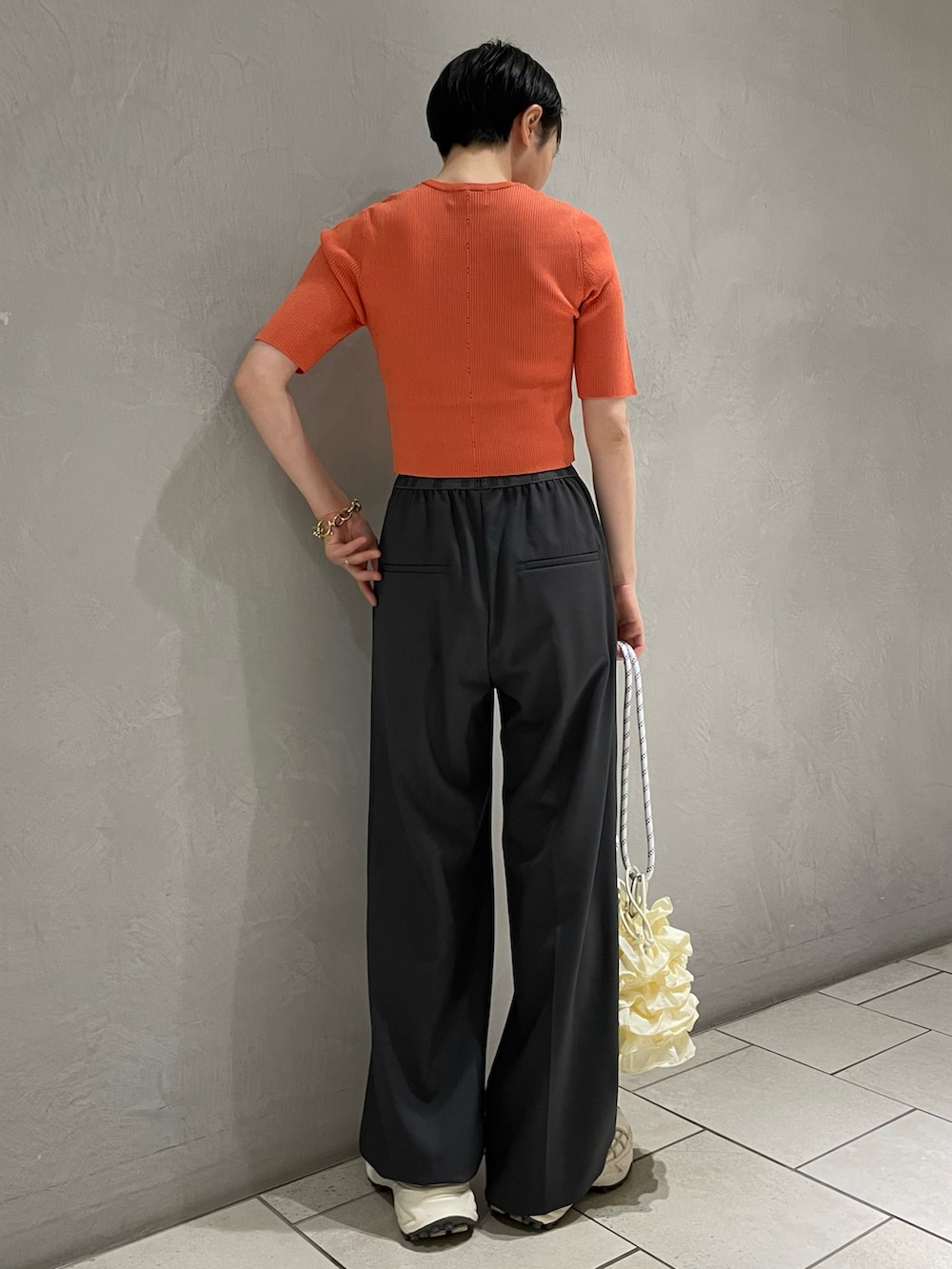 グレー系のスラックス、オレンジ系のニット/セーター、ホワイト系のショルダーバッグを着用したレディースの夏コーディネートの2枚目の写真