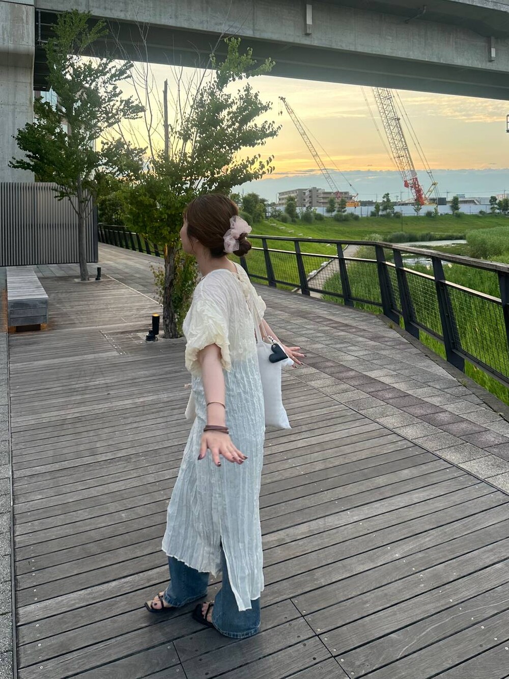 ベージュ系のショルダーバッグ、ブルー系のデニムパンツ、ホワイト系のワンピースを着用したレディースの夏コーディネートの2枚目の写真