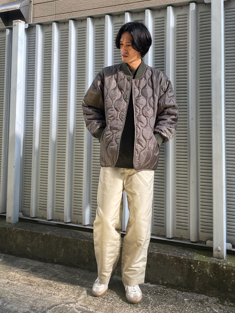 グリーン系のニット/セーター、グリーン系のミリタリージャケット、ベージュ系のパンツを着用したメンズの秋コーディネートの2枚目の写真