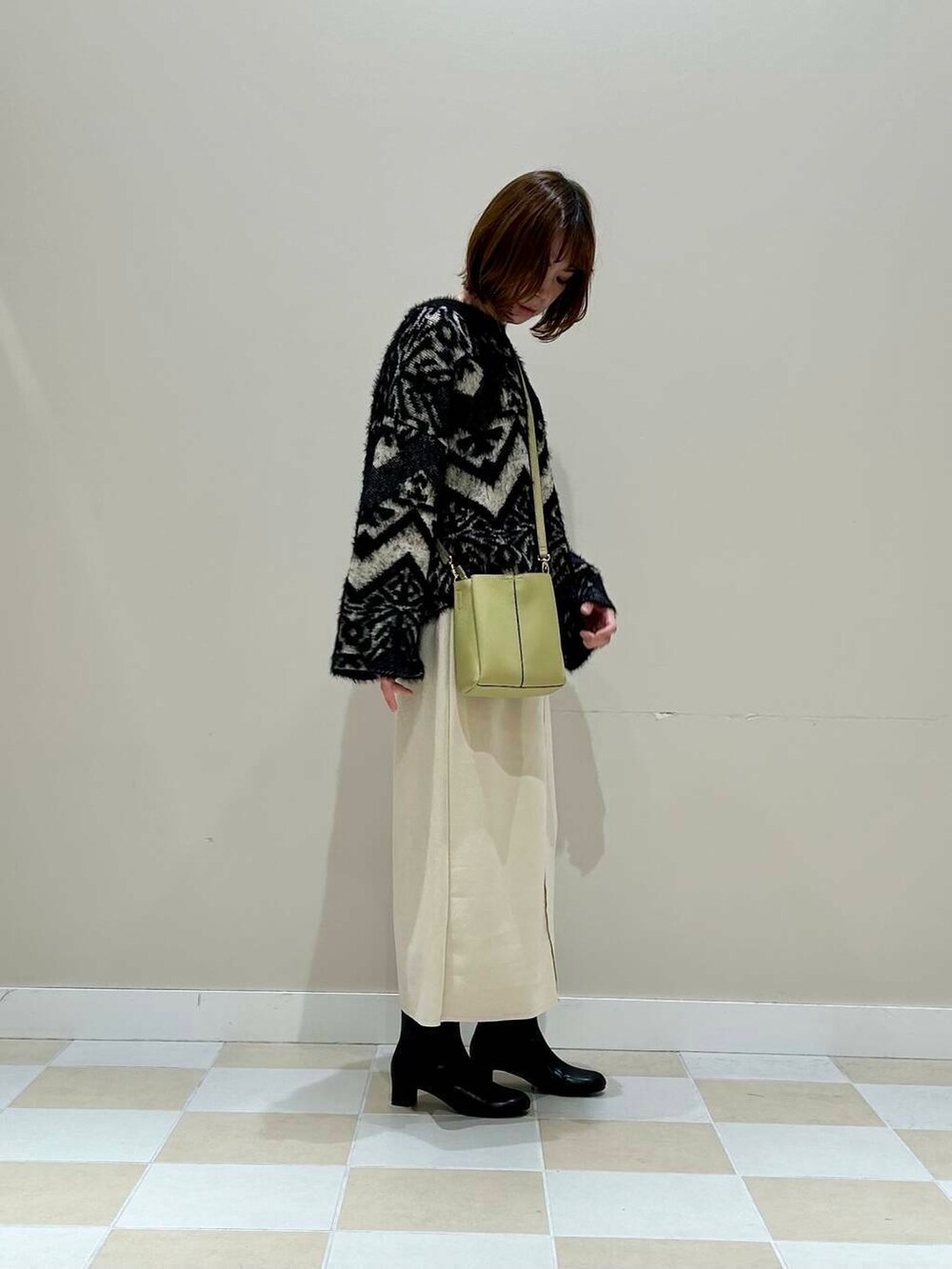 ブラック系のブーツ、グリーン系のショルダーバッグ、ホワイト系のスカートを着用したレディースの冬コーディネートの2枚目の写真