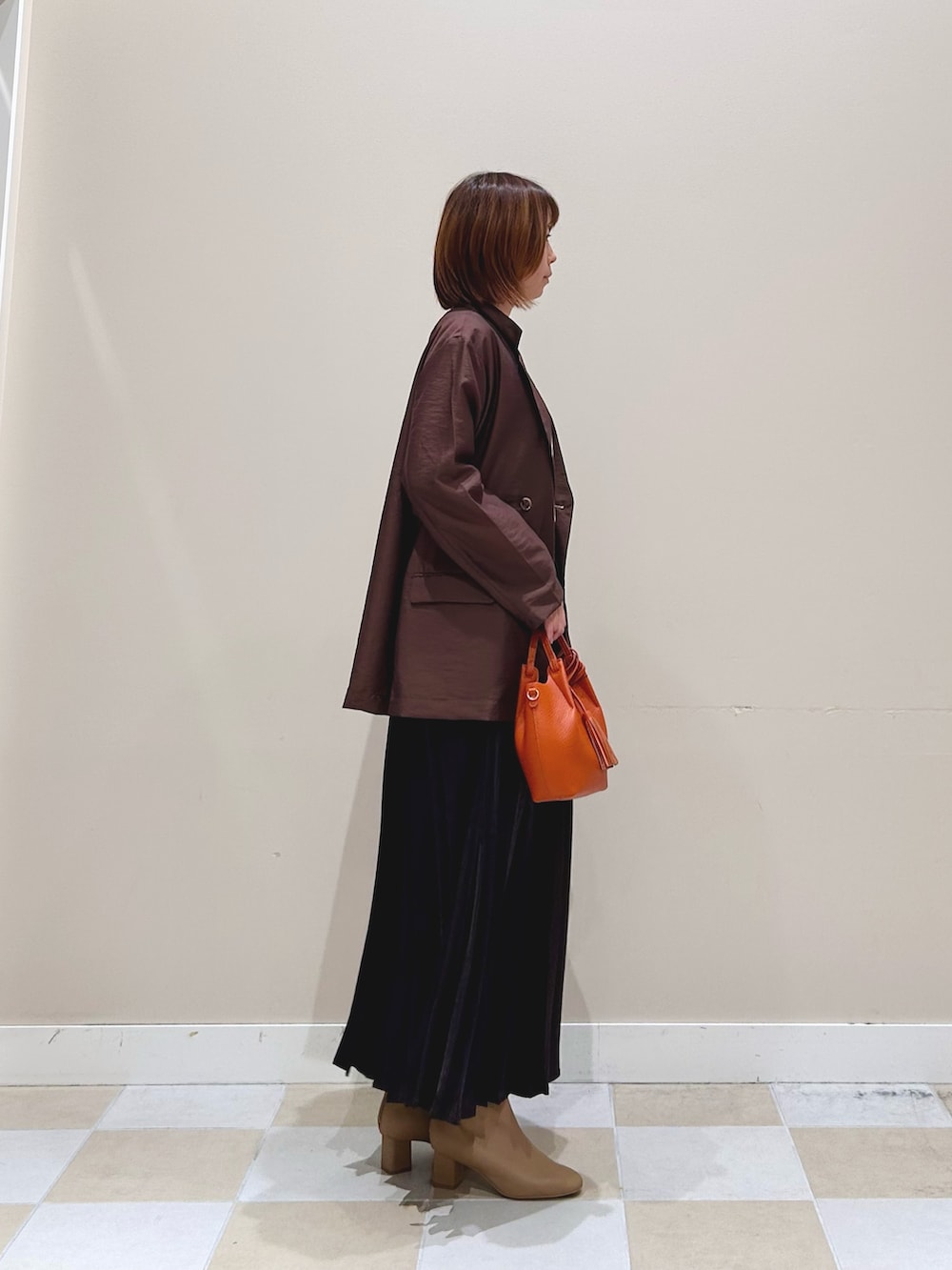 オレンジ系のショルダーバッグ、グレー系のスカート、ブラウン系のその他アウターを着用したレディースの秋コーディネートの2枚目の写真