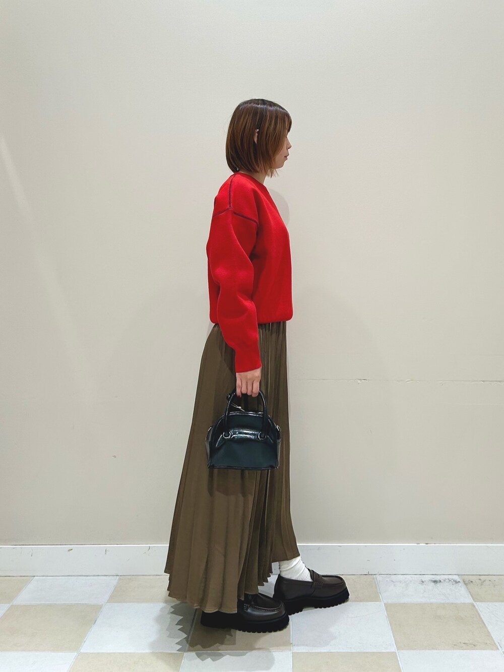 レッド系のニット/セーター、ブラウン系のスカート、ブラック系のボストンバッグを着用したレディースの秋コーディネートの2枚目の写真