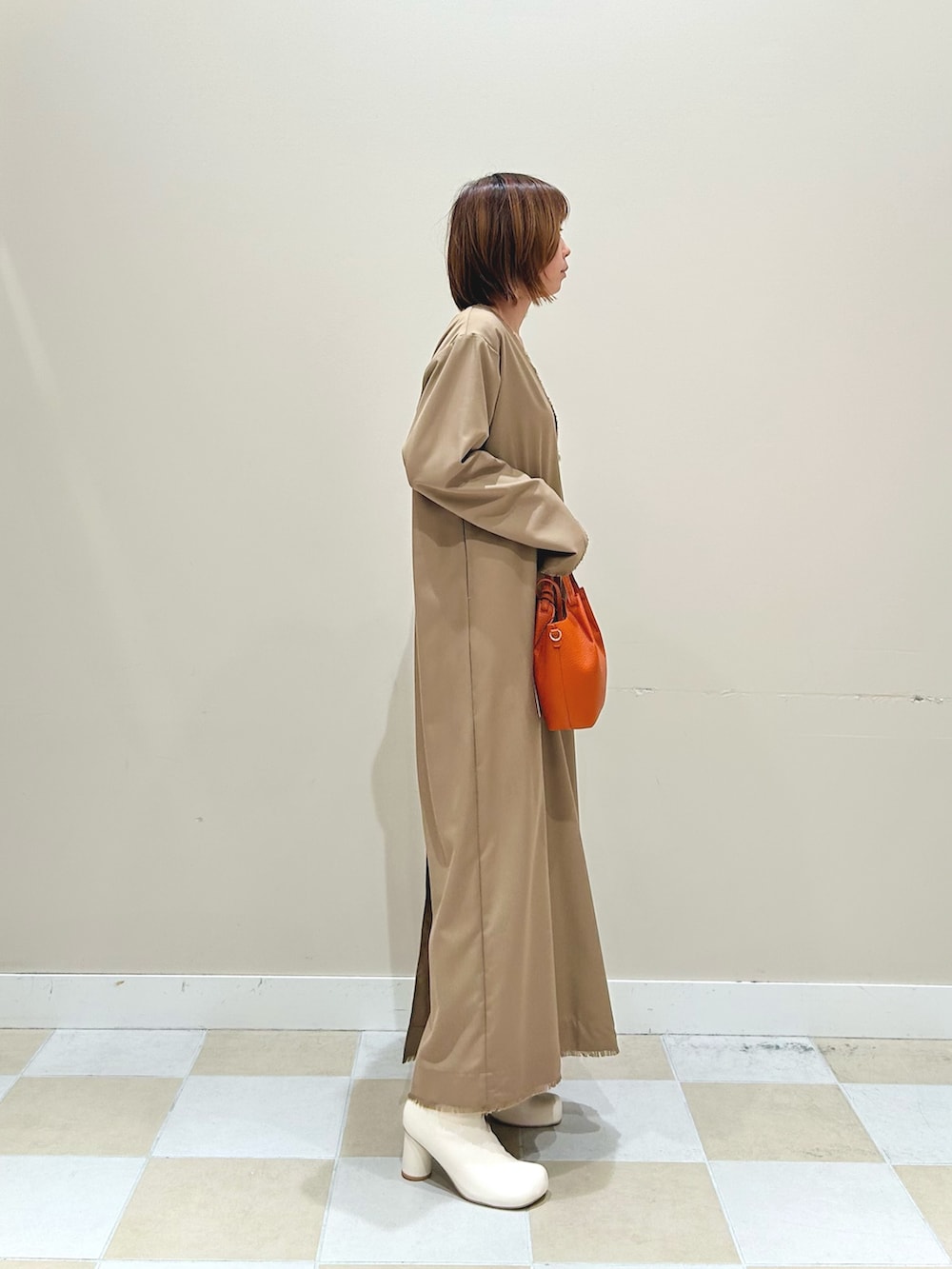 オレンジ系のショルダーバッグ、ベージュ系のワンピースを着用したレディースの秋コーディネートの2枚目の写真