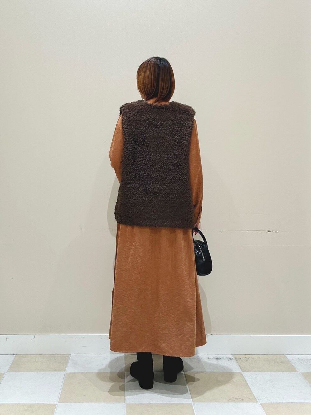 オレンジ系のワンピース、ブラウン系のベスト、ブラック系のボストンバッグを着用したレディースの秋コーディネートの2枚目の写真