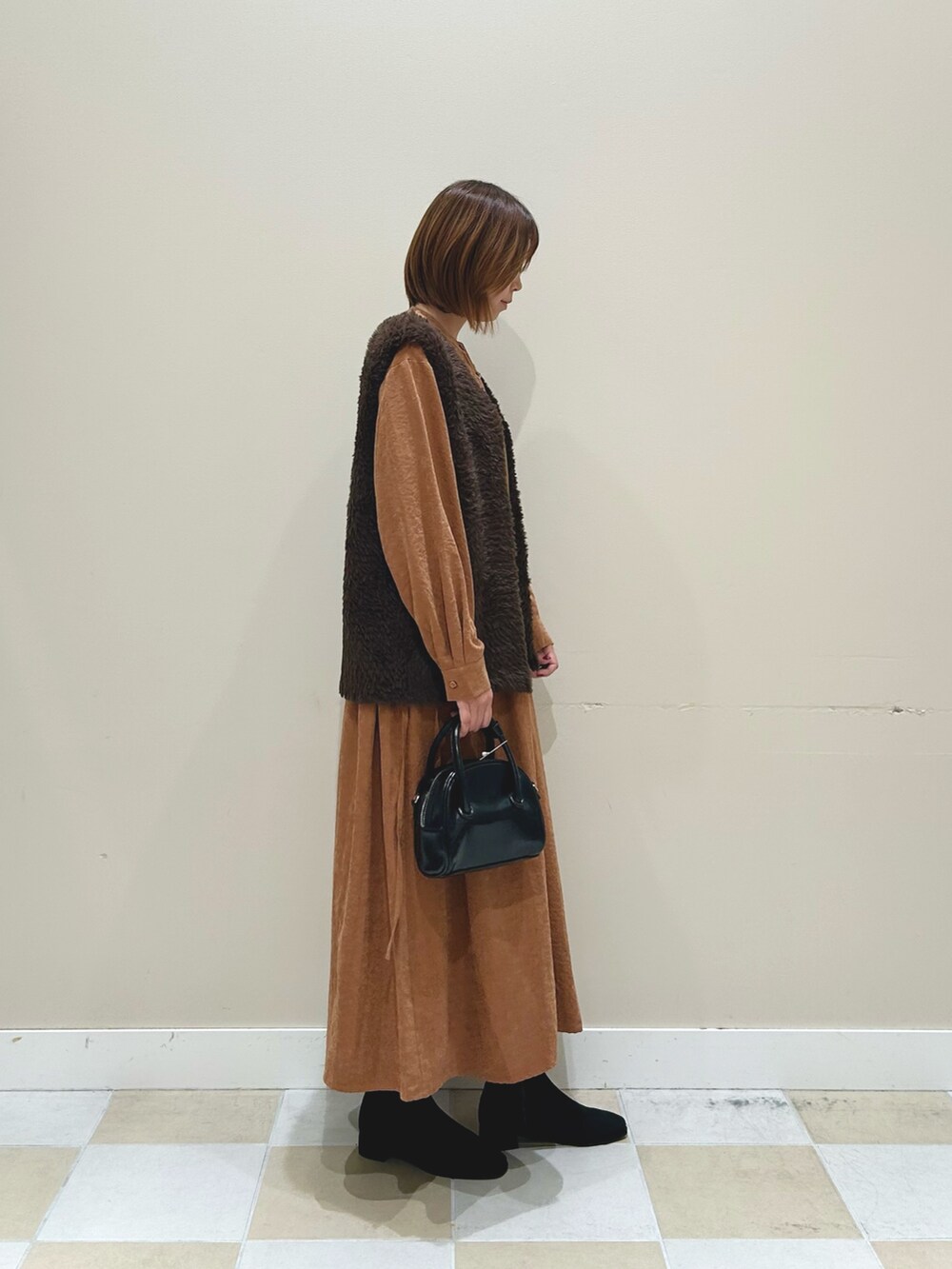 オレンジ系のワンピース、ブラウン系のベスト、ブラック系のボストンバッグを着用したレディースの秋コーディネートの3枚目の写真