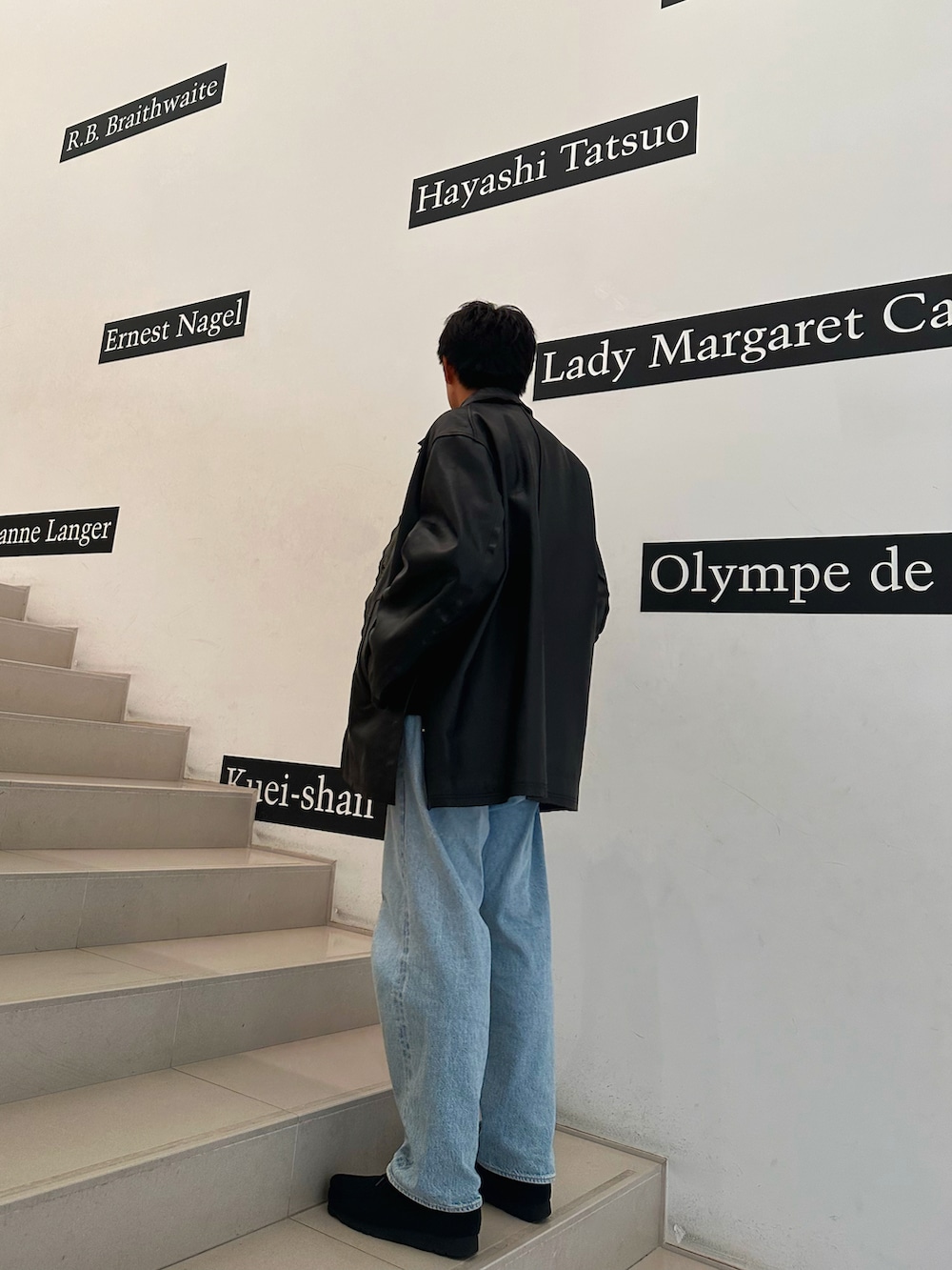 ブラック系のその他アウター、ブルー系のデニムパンツ、ブラック系のモカシン/デッキシューズを着用したメンズの秋コーディネートの2枚目の写真