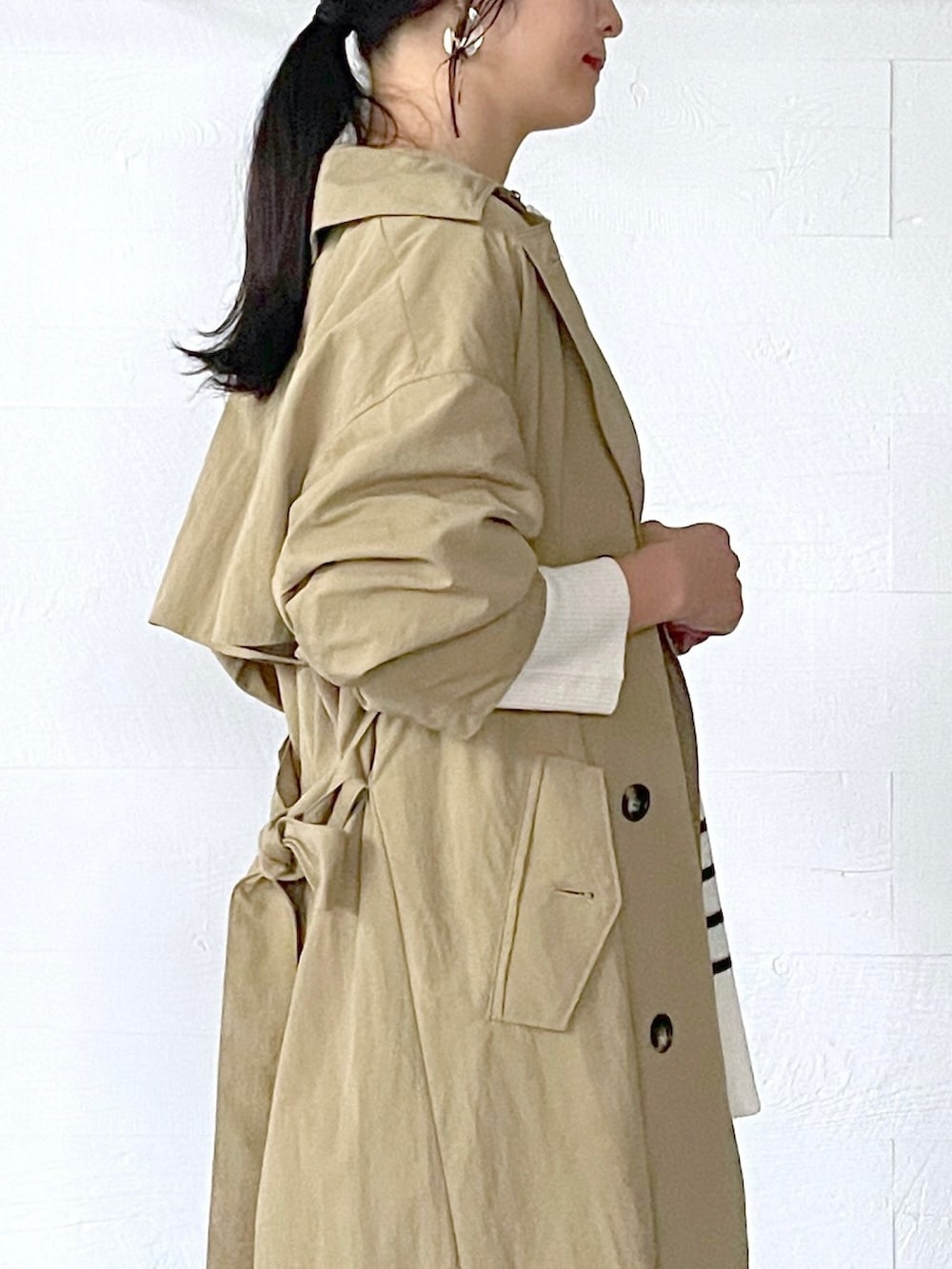 ベージュ系のトレンチコート、ホワイト系のニット/セーター、ブルー系のデニムパンツを着用したレディースの秋コーディネートの4枚目の写真