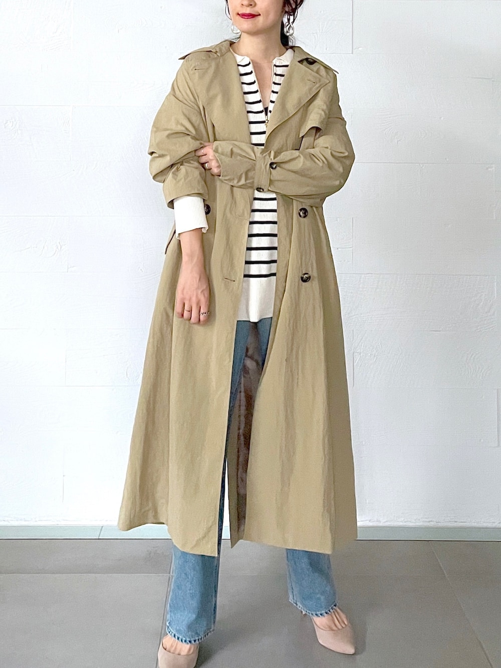 ベージュ系のトレンチコート、ホワイト系のニット/セーター、ブルー系のデニムパンツを着用したレディースの秋コーディネートの5枚目の写真