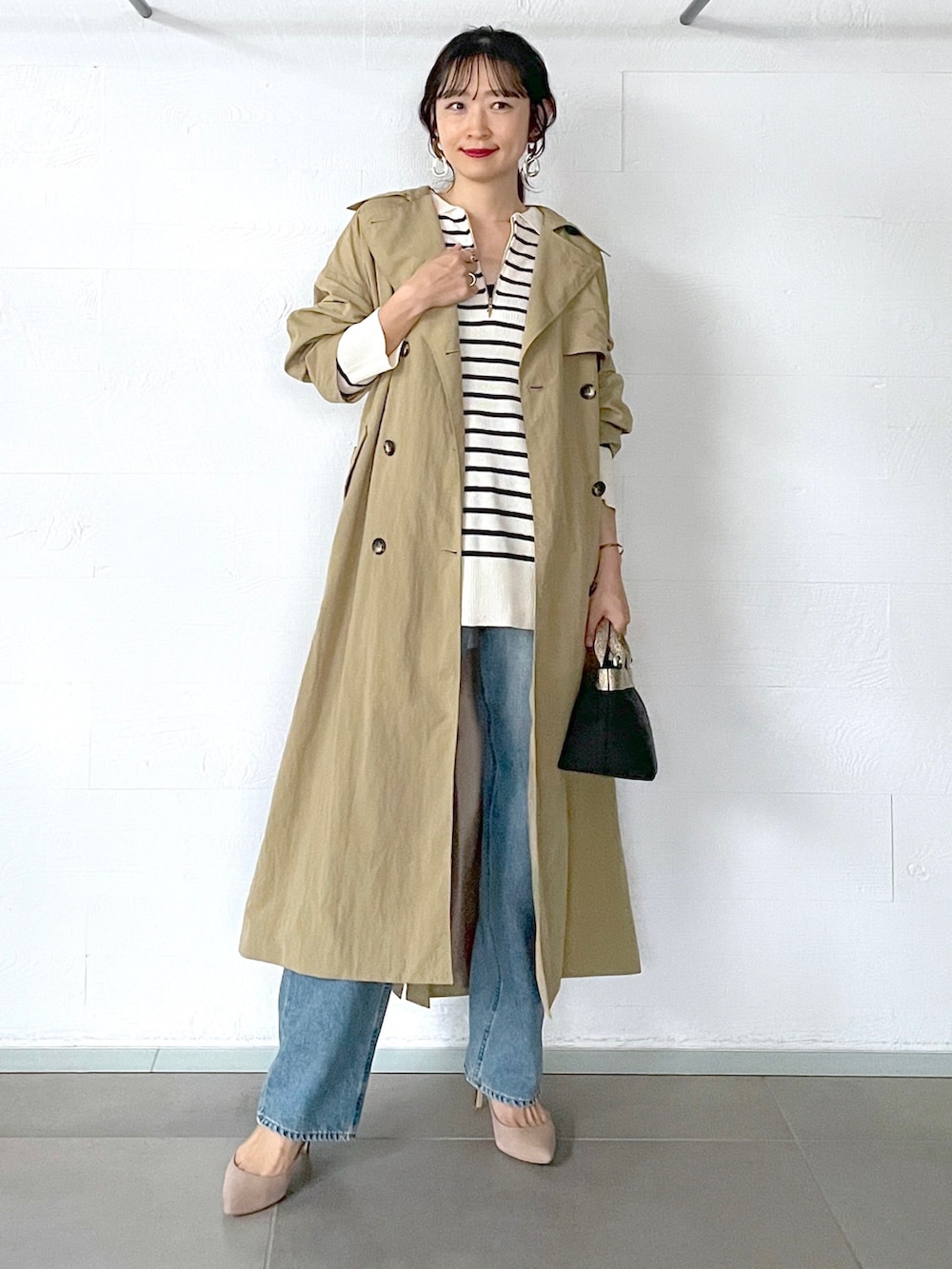 ベージュ系のトレンチコート、ホワイト系のニット/セーター、ブルー系のデニムパンツを着用したレディースの秋コーディネートの2枚目の写真