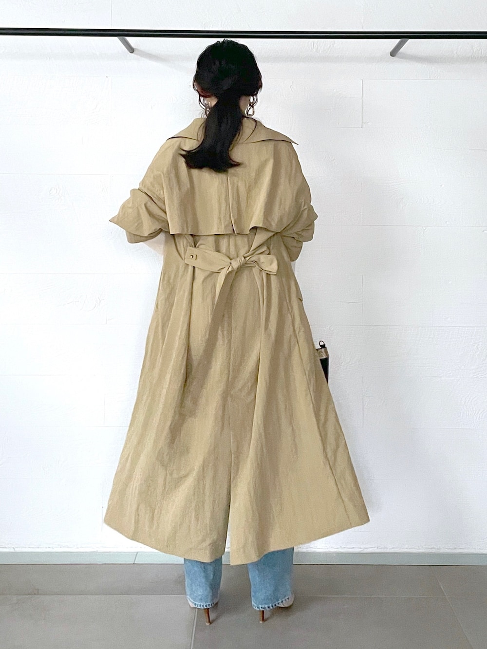 ベージュ系のトレンチコート、ホワイト系のニット/セーター、ブルー系のデニムパンツを着用したレディースの秋コーディネートの3枚目の写真