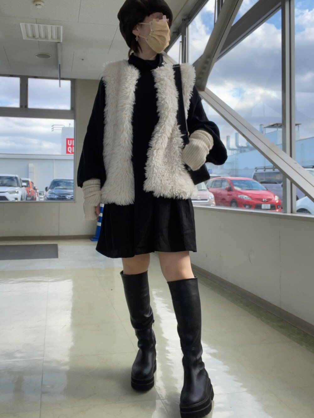 ブラック系のブーツ、ホワイト系のベスト、ブラック系のワンピースを着用したレディースの冬コーディネートの3枚目の写真