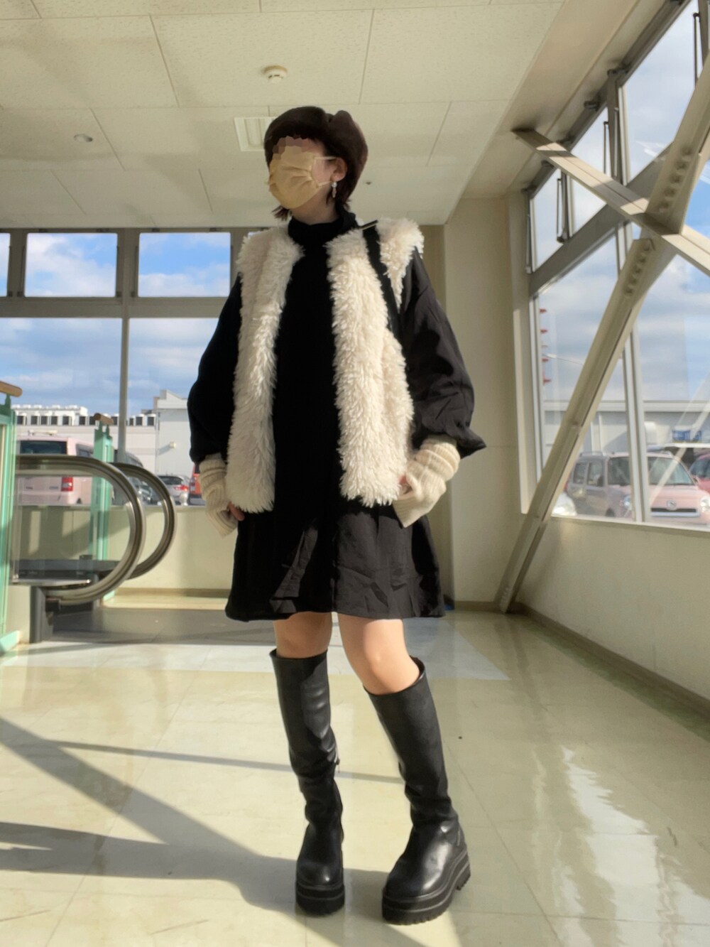 ブラック系のブーツ、ホワイト系のベスト、ブラック系のワンピースを着用したレディースの冬コーディネートの2枚目の写真