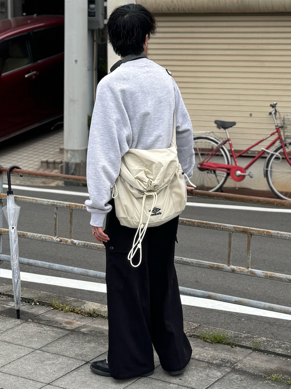 ブラック系のスラックス、ブラック系のスニーカー、ホワイト系のショルダーバッグを着用したメンズの春コーディネートの2枚目の写真