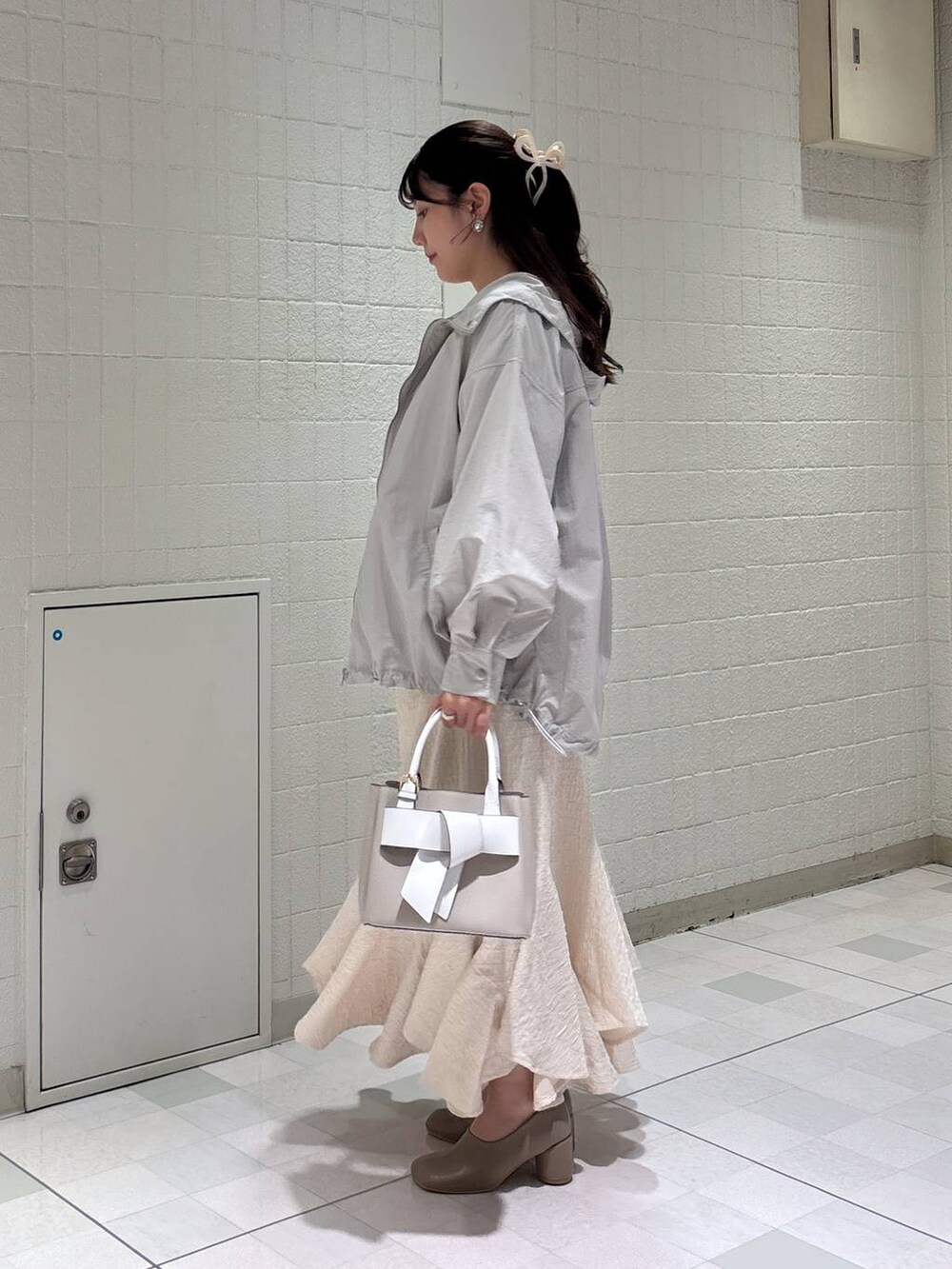 ホワイト系のスカート、ベージュ系のショルダーバッグ、グレー系のマウンテンパーカーを着用したレディースの春コーディネートの2枚目の写真