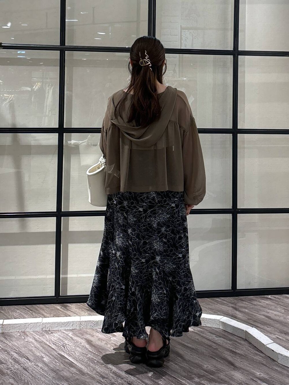 ホワイト系のハンドバッグ、ブラウン系のパーカー、ブラック系のスカートを着用したレディースの夏コーディネートの3枚目の写真