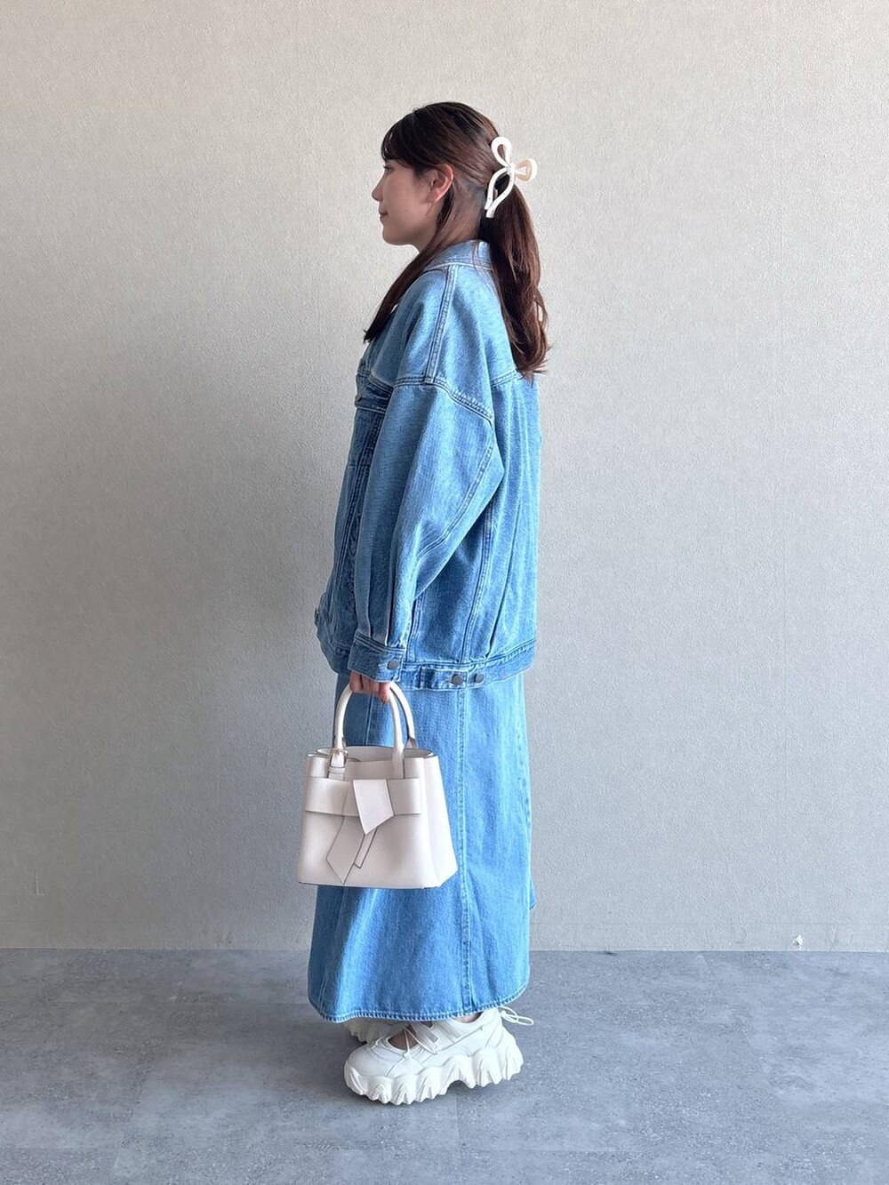 ブルー系のデニムジャケット、ブルー系のジャンパースカート、ホワイト系のショルダーバッグを着用したレディースの冬コーディネートの2枚目の写真