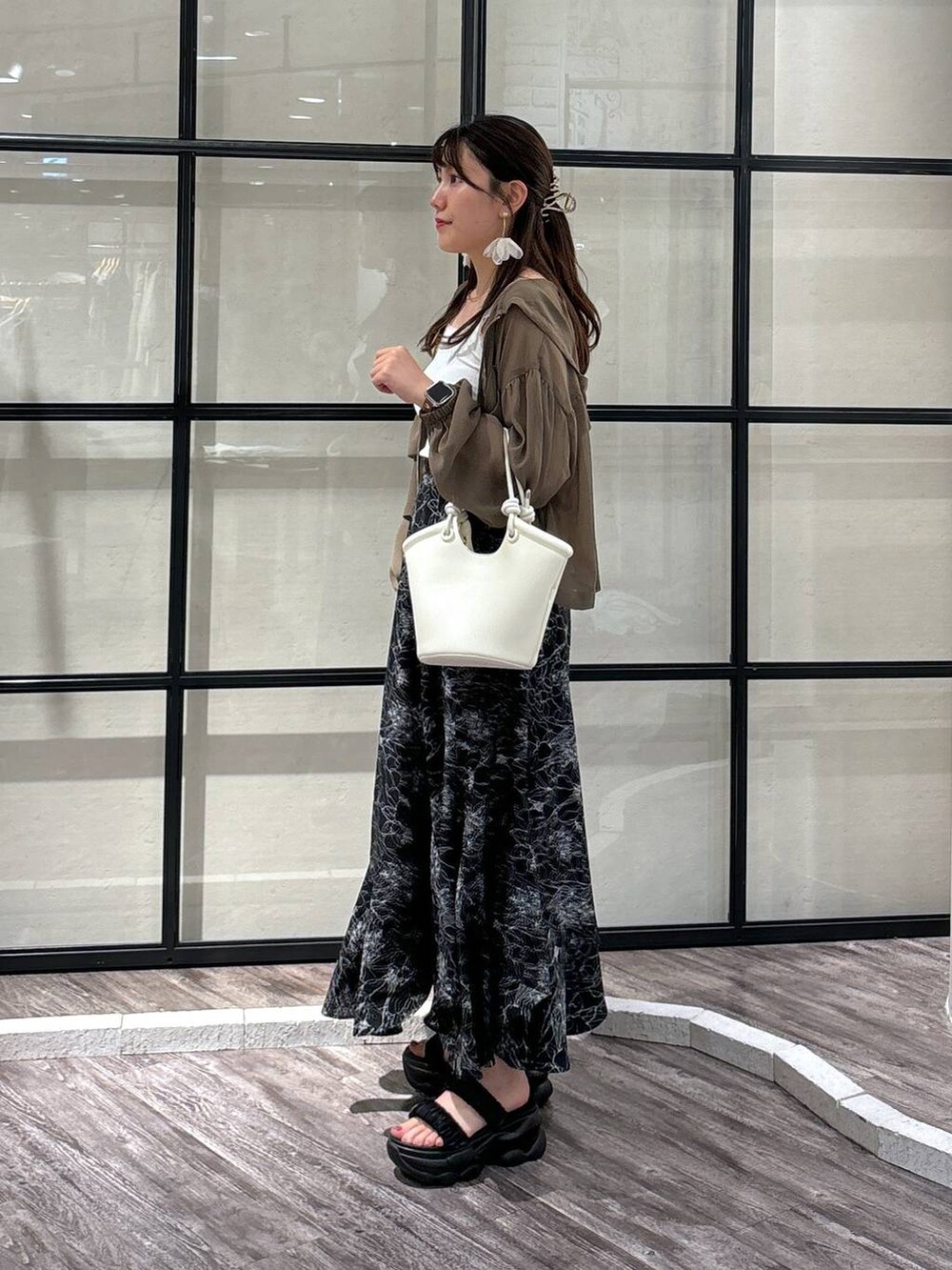 ホワイト系のハンドバッグ、ブラウン系のパーカー、ブラック系のスカートを着用したレディースの夏コーディネートの2枚目の写真