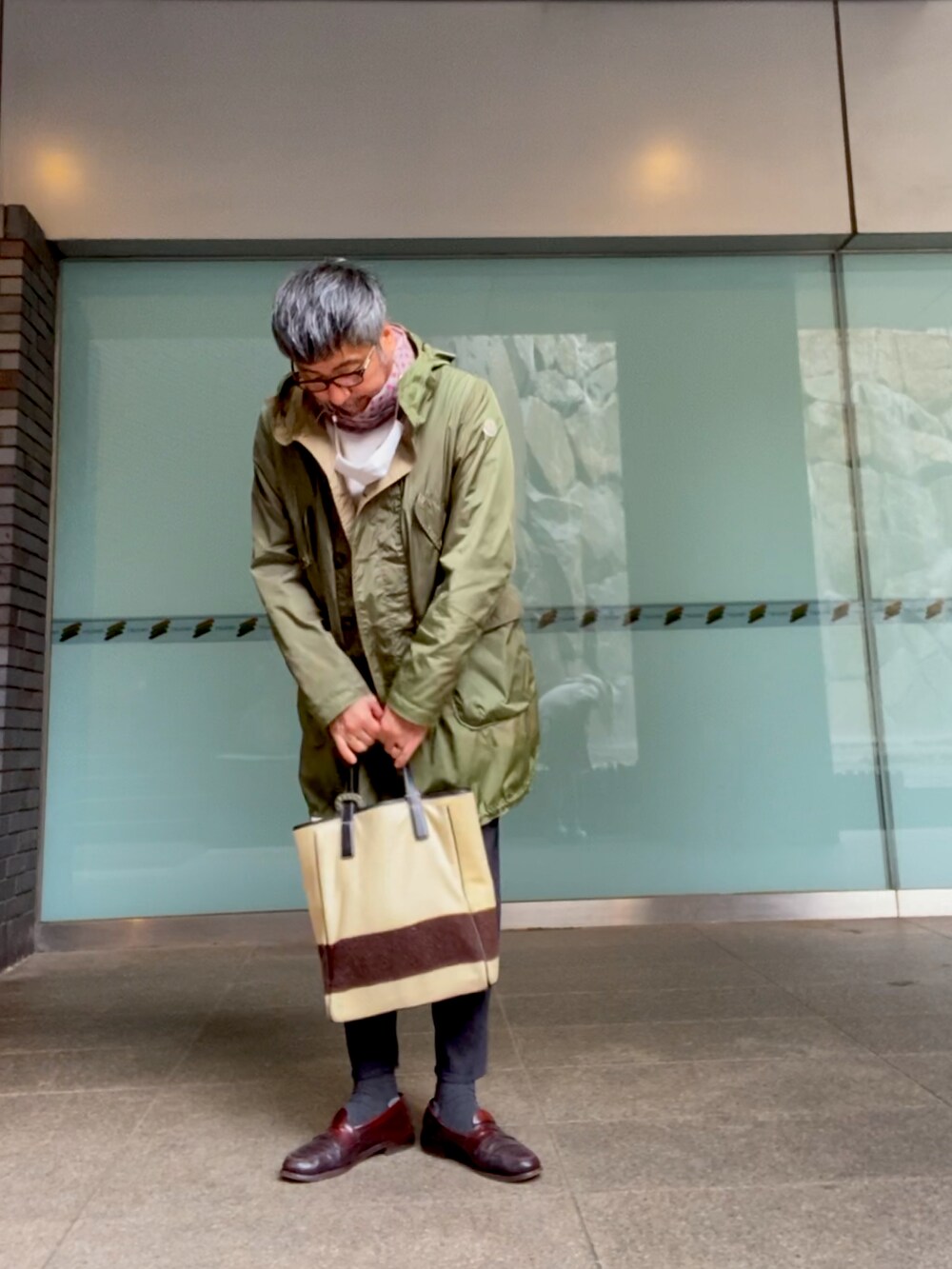 グリーン系のモッズコート、ブルー系のデニムパンツ、ベージュ系のトートバッグを着用したメンズの冬コーディネートの2枚目の写真