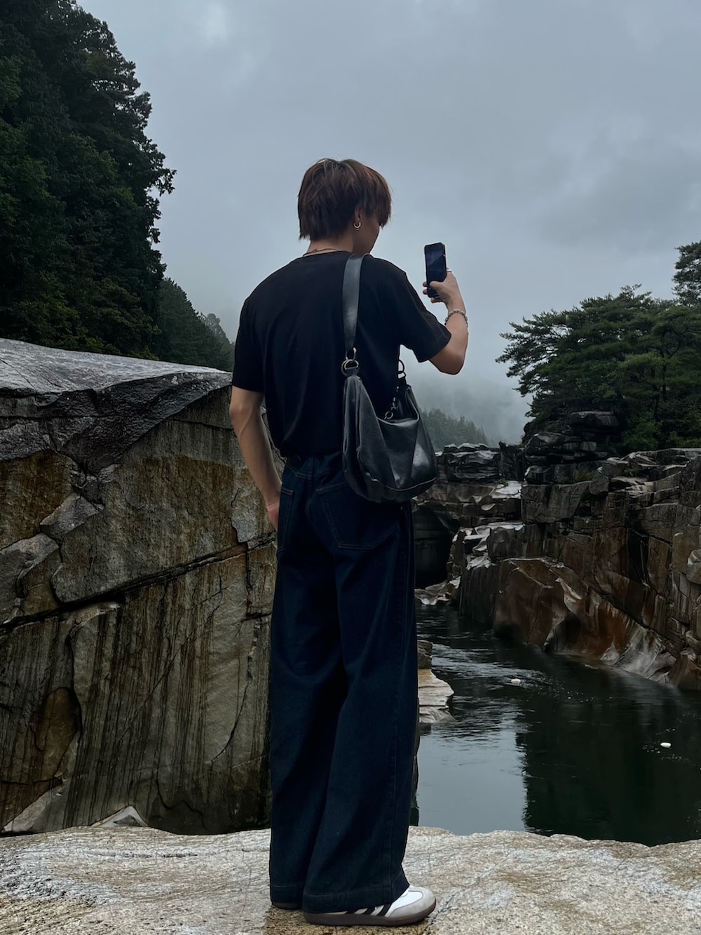 ブルー系のデニムパンツ、ブラック系のショルダーバッグ、ホワイト系のスニーカーを着用したメンズの秋コーディネートの3枚目の写真