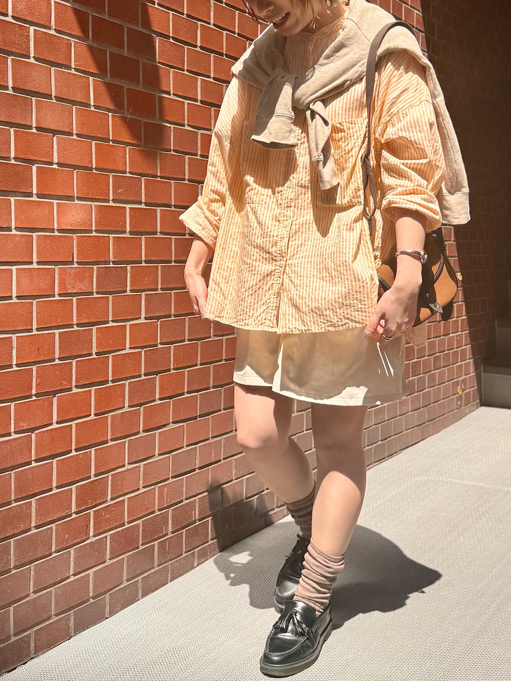 オレンジ系のシャツ/ブラウス、ブラック系のローファー、ブラウン系のショルダーバッグを着用したレディースの春コーディネートの2枚目の写真